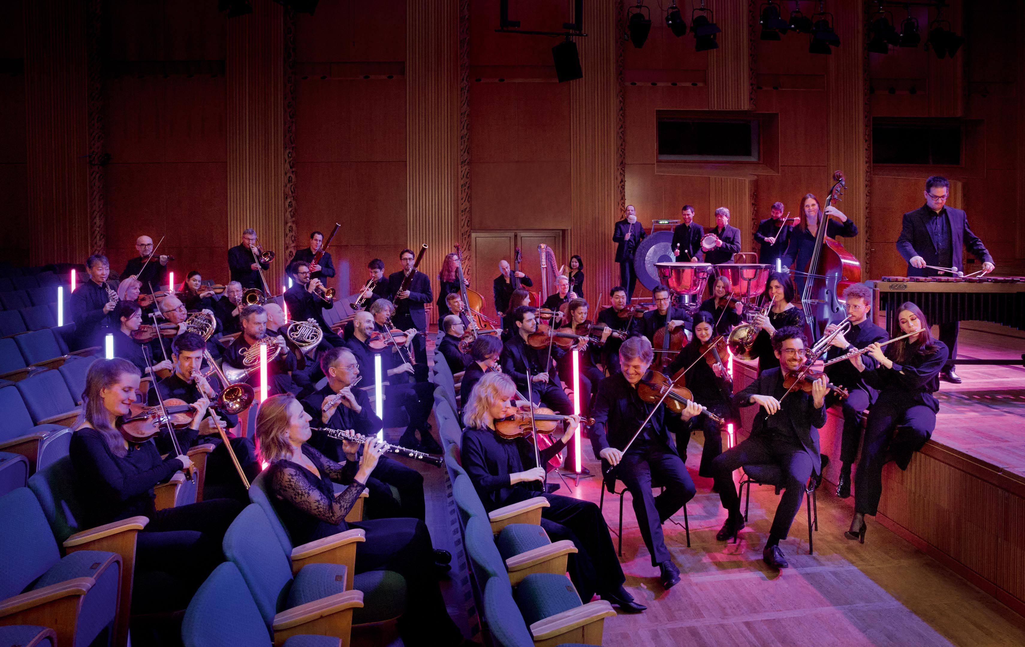 Das Ensemble des WDR-Funkhausorchesters sitzt in den Stuhlreihen eines Konzerthauses.
