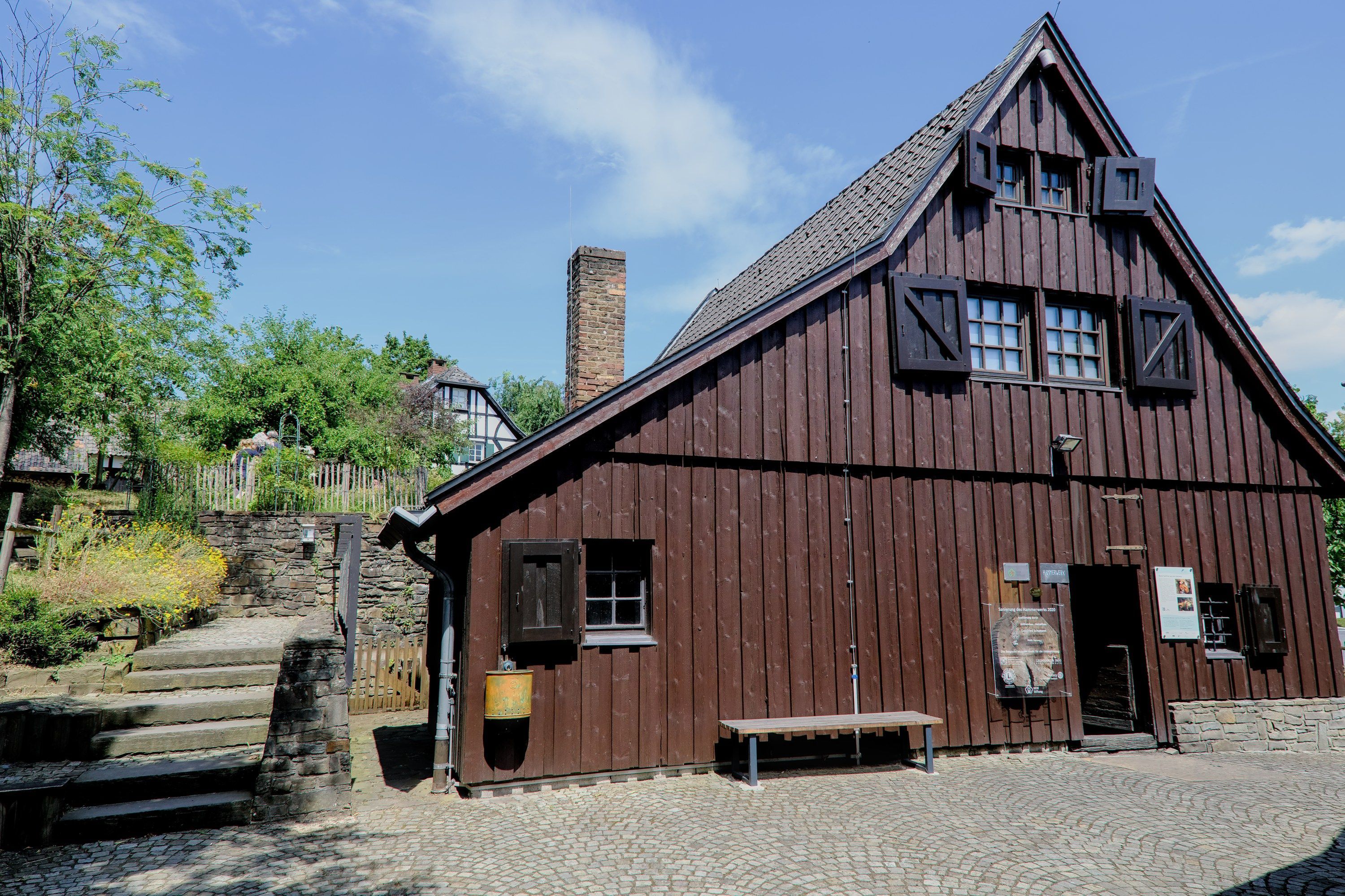 Eine Fassade eines großen mit Holz verkleideten Hauses, davor eine Bank