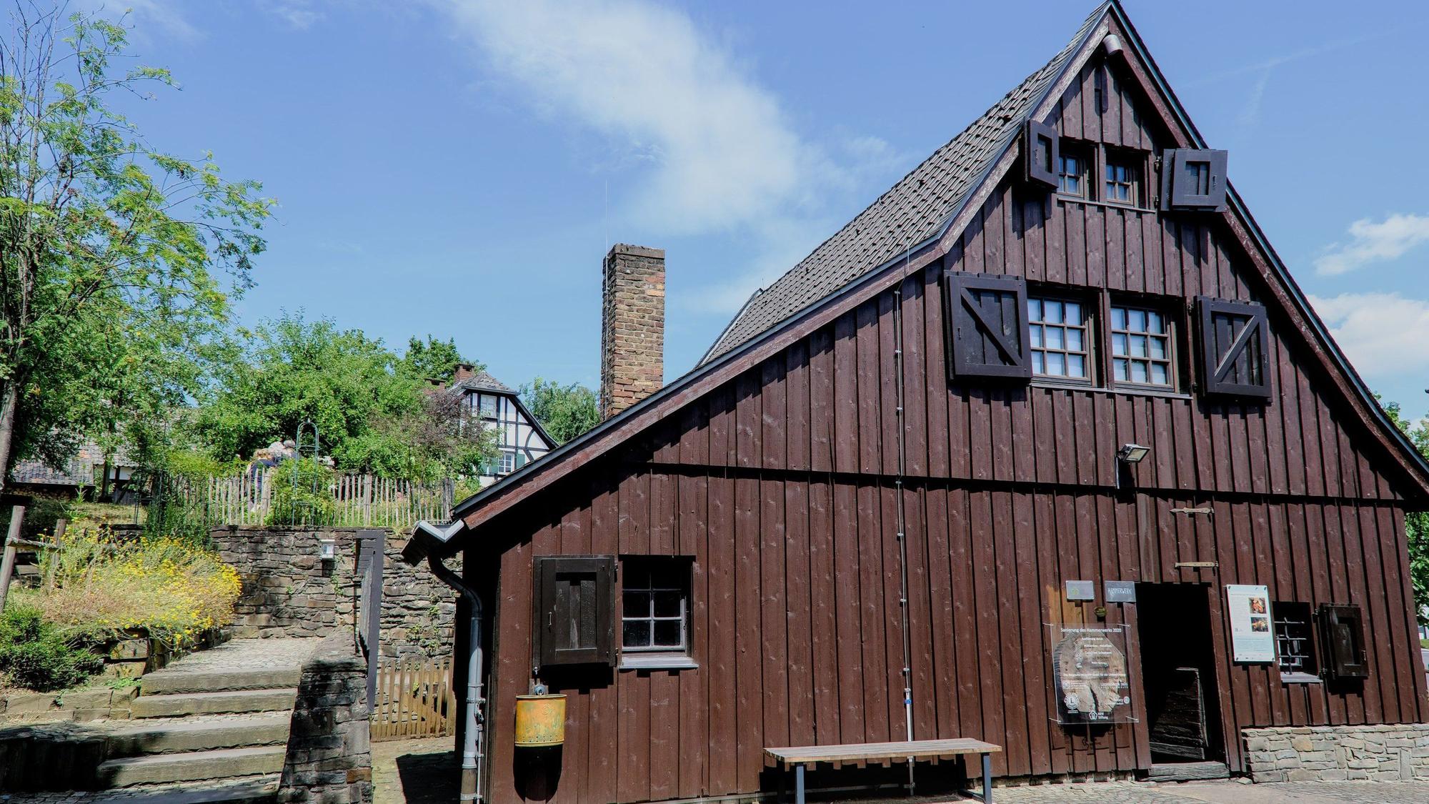 Eine Fassade eines großen mit Holz verkleideten Hauses, davor eine Bank