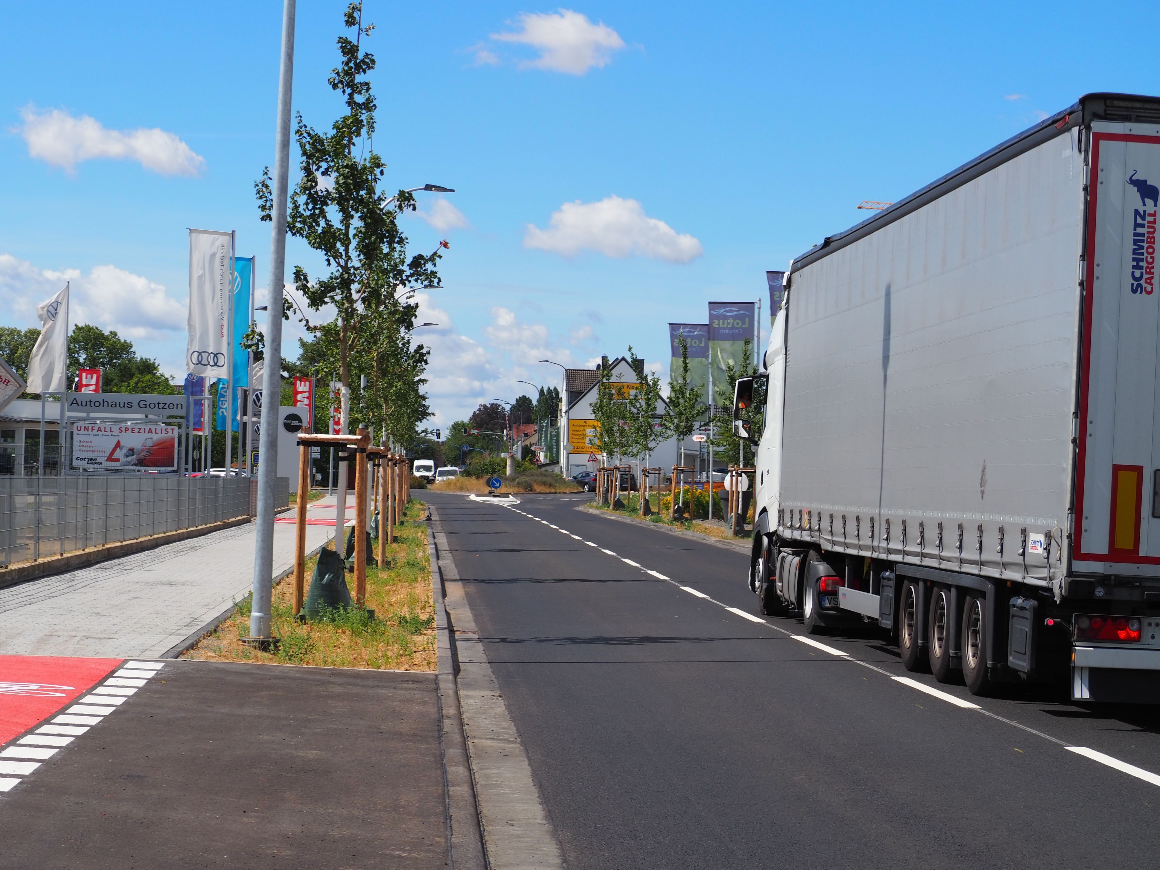 Auf der sanierten Römerallee fährt ein Lastwagen. Links steht eine Reihe Schwammstadtbäume.