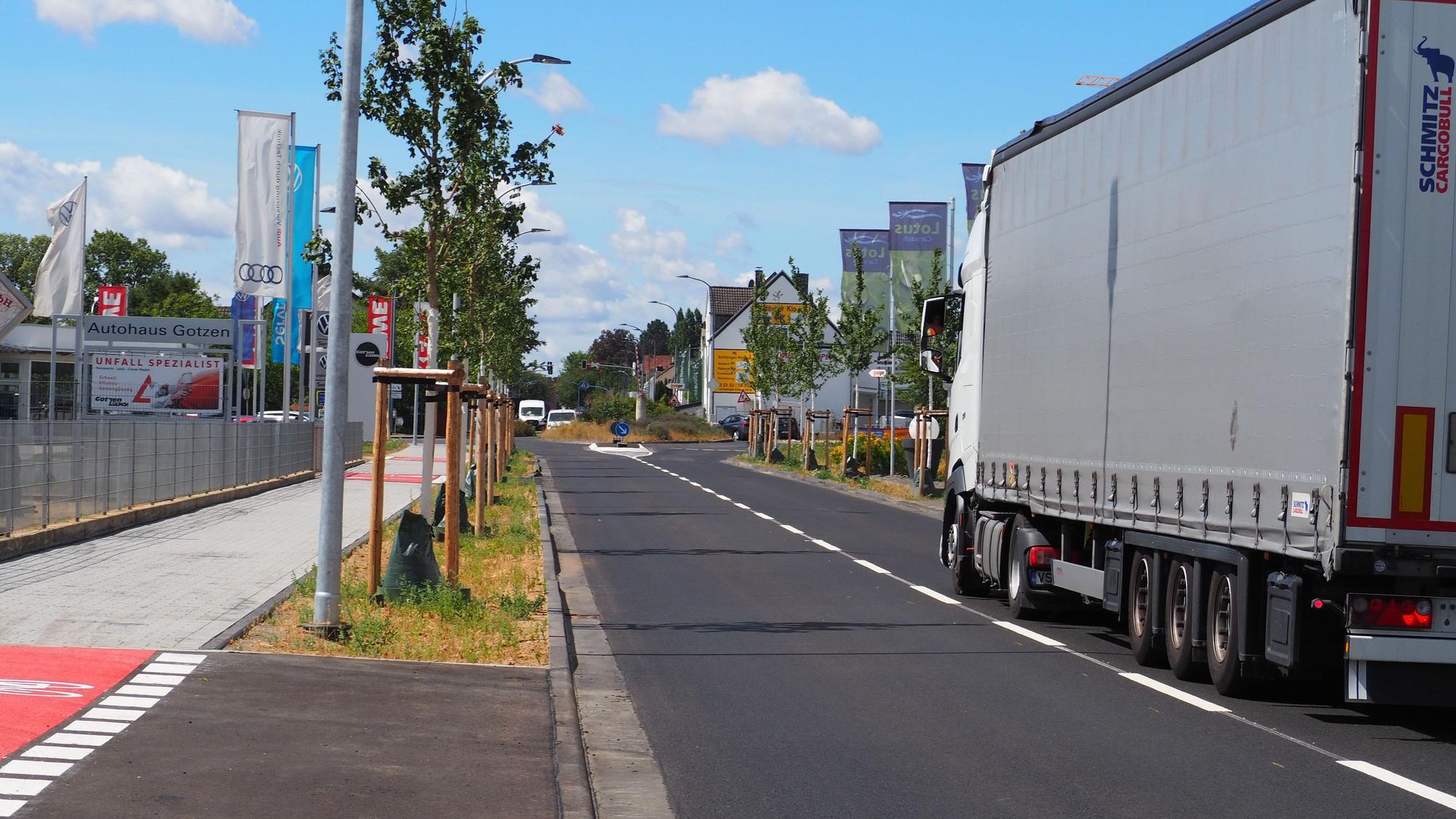 Auf der sanierten Römerallee fährt ein Lastwagen. Links steht eine Reihe Schwammstadtbäume.