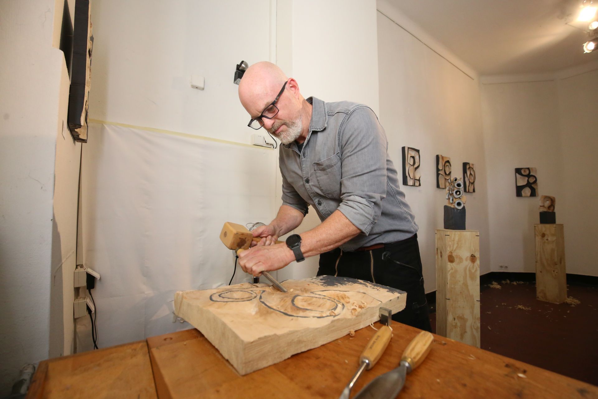 Ein Man arbeitet mit Hammer und Beitel an seiner Holzplatte.