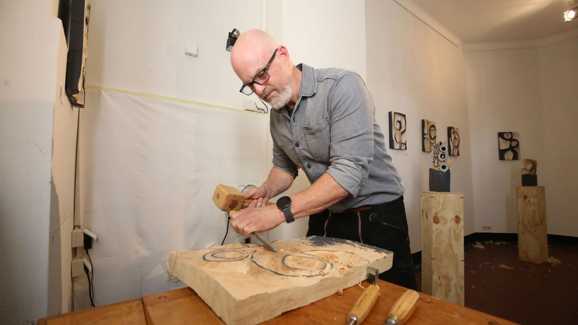 Ein Man arbeitet mit Hammer und Beitel an seiner Holzplatte.