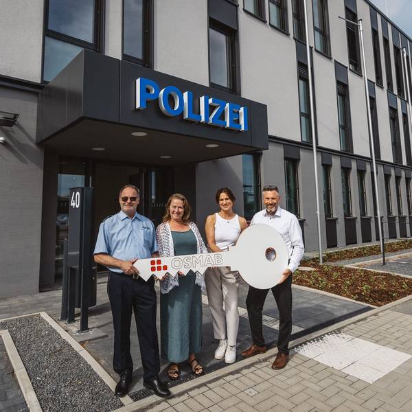 Auf dem Bild sind zwei Frauen und zwei Männer vor dem neuen Polizeigebäude zu sehen, sie halten einen großen symbolischen Schlüssel in der Hand.