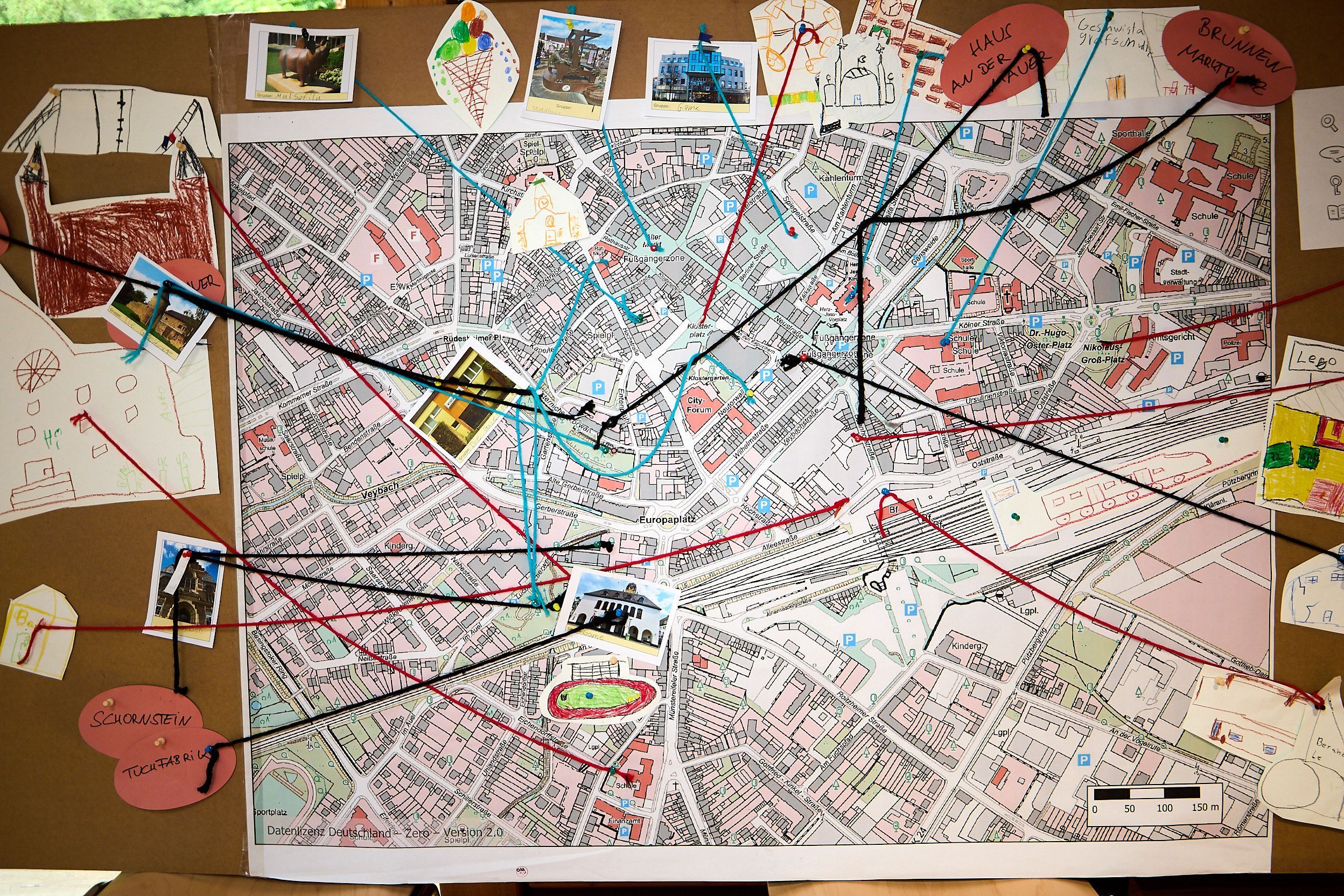 Auf einem großen Stadtplan von Euskirchen sind einige Orte mit Fotos und Wollfäden markiert.