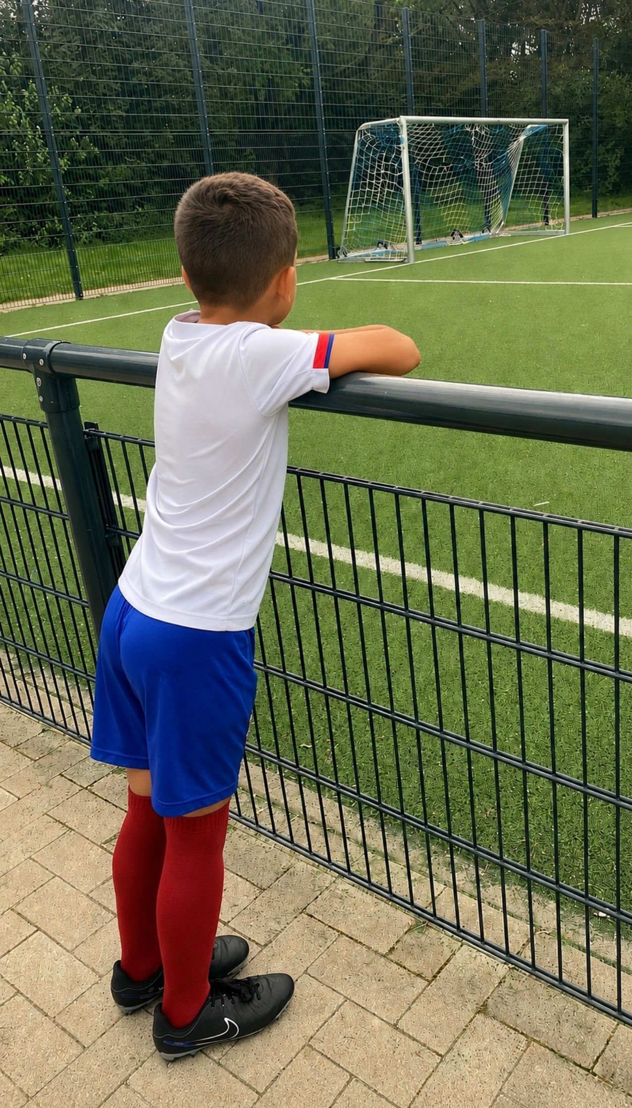 Junge schaut über einen Zaun auf einen Fußballplatz.