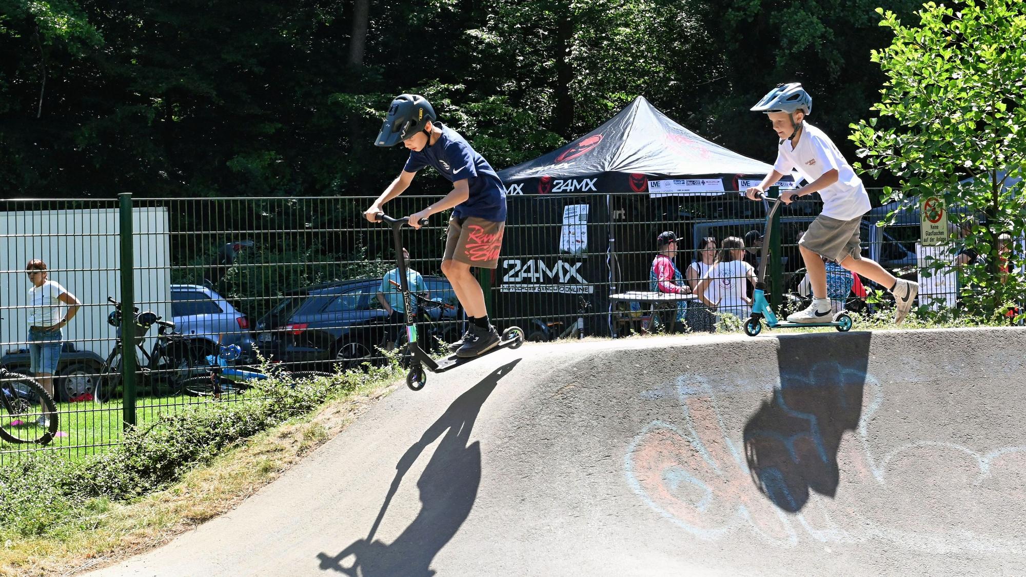Die beiden Jungs befahren den Pumptrack in Kommern mit ihren City-Rollern.