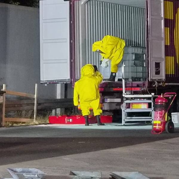 Das Bild zeigt zwei Feuerwehrleute, die unter großen Vorsichtsmaßnahmen die Container untersuchen.