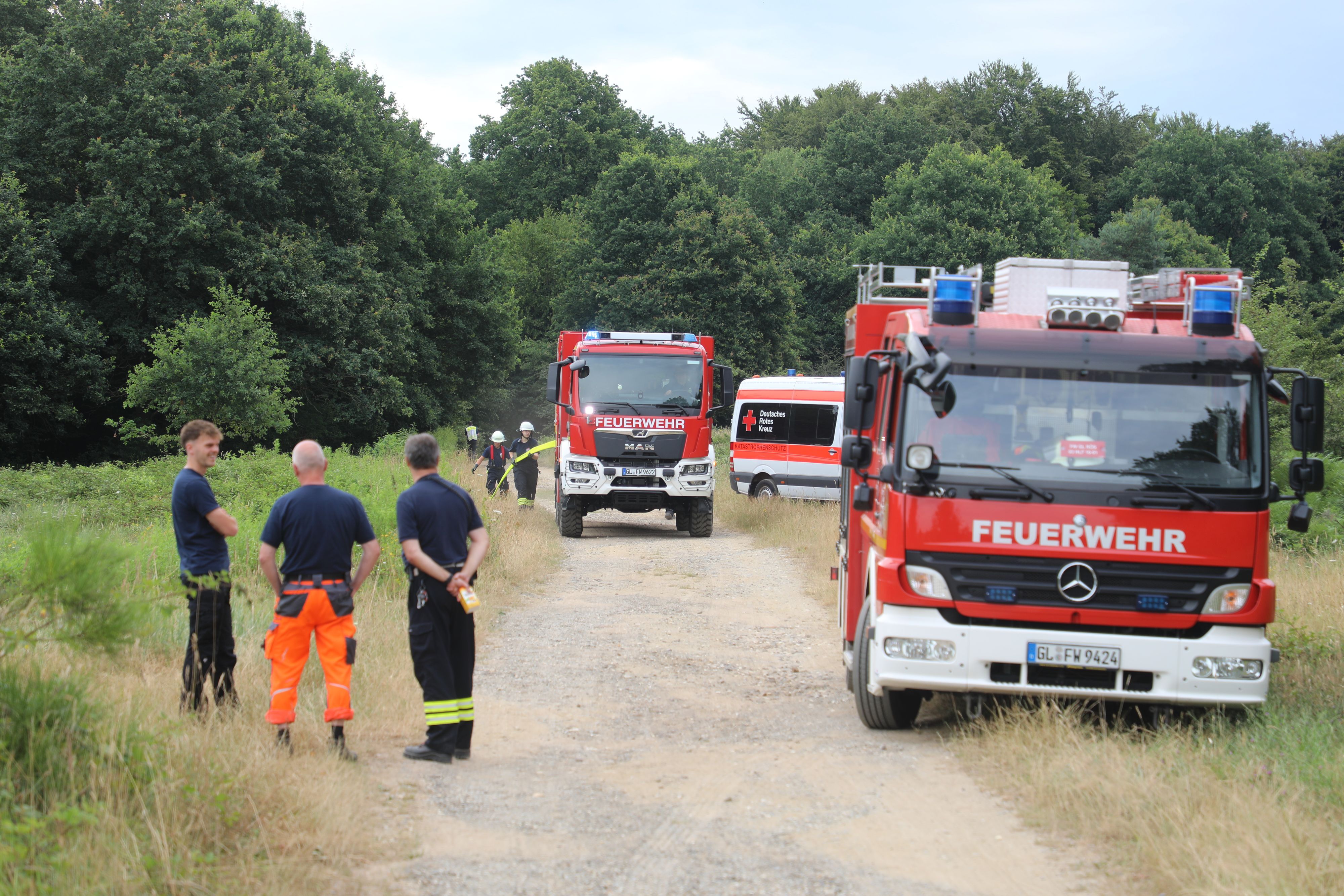 Zwei Feuerwehrautos und drei Männer der Feuerwehr auf einem Schotterweg.