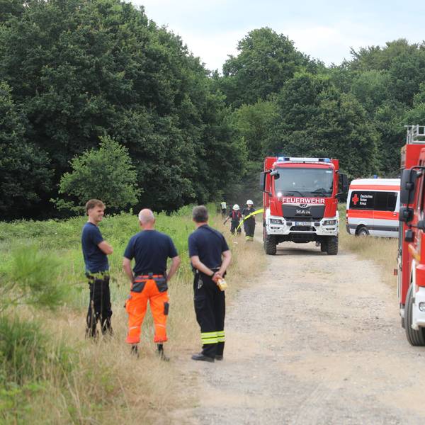 Zwei Feuerwehrautos und drei Männer der Feuerwehr auf einem Schotterweg.