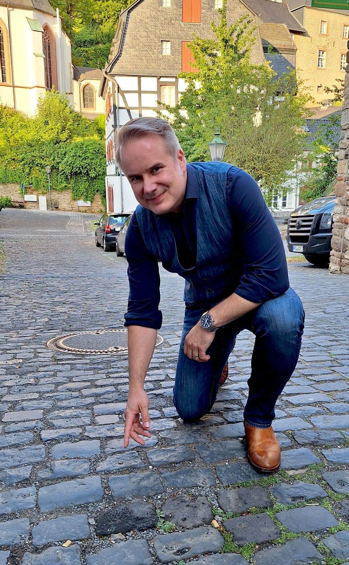 Bernd Niedermeier kniet auf dem Kopfsteinpflaster und deutet auf einen Stein.