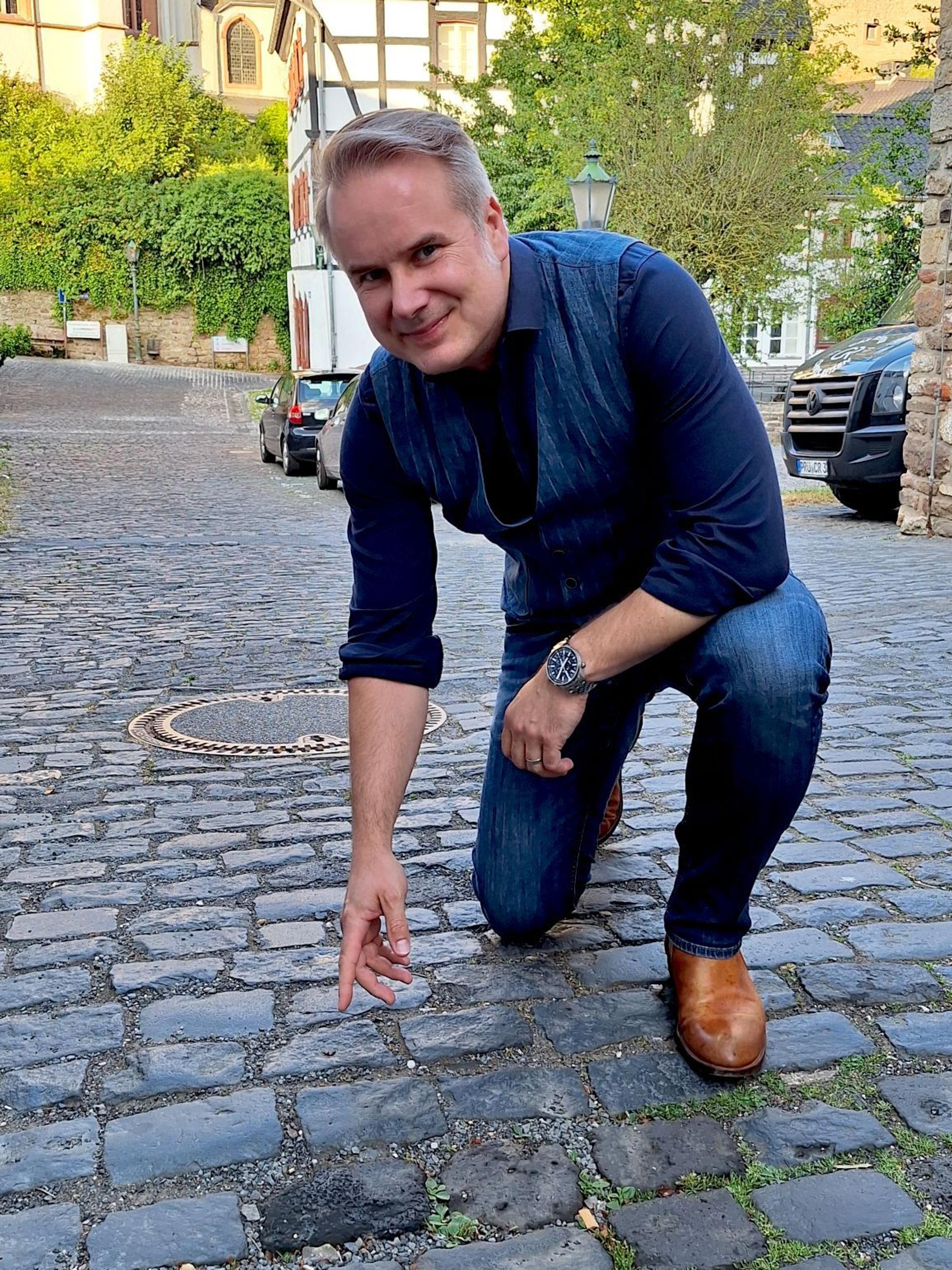 Bernd Niedermeier kniet auf dem Kopfsteinpflaster und deutet auf einen Stein.