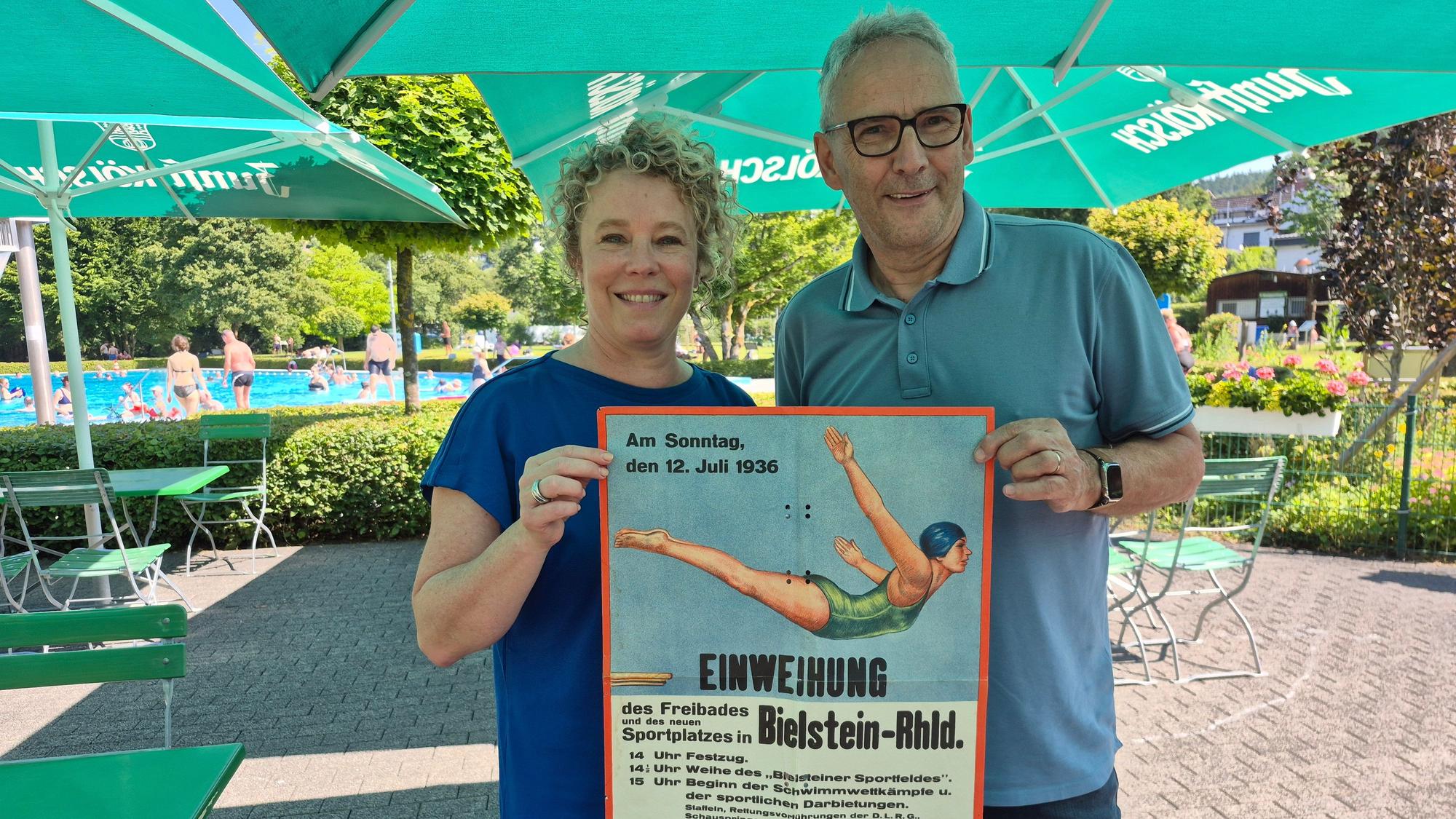 Das Foto zeigt links Nicole Klein und rechts Andreas Zurek mit einem alten Plakat vom Einweihungsfest vor 90 Jahren.