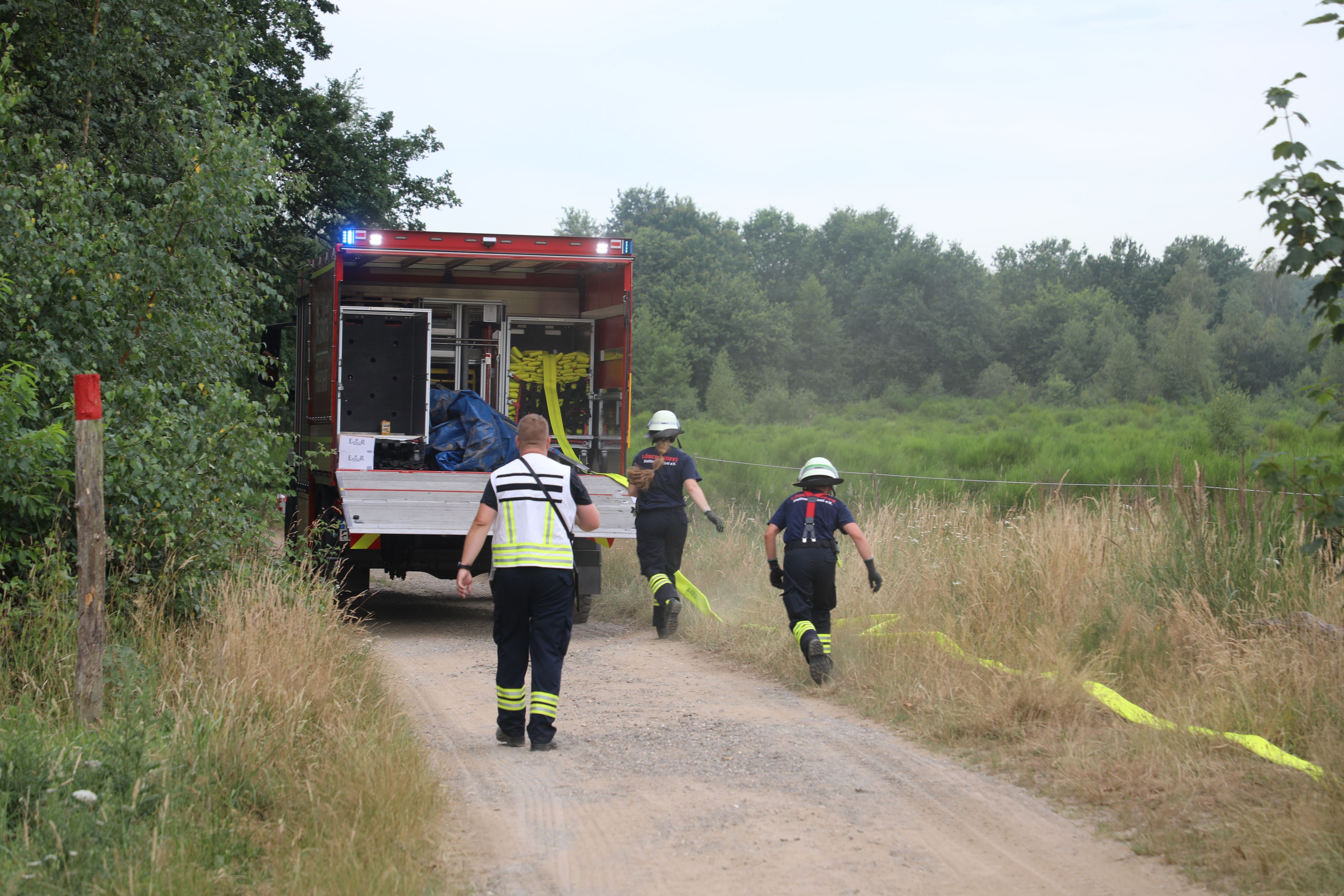 Feuerwehrleute verlegen von einem Schlauchwagen einen B-Schlauch zur Wasserversorgung der Einsatzstelle an einem Waldbrand in der Wahner Heide.