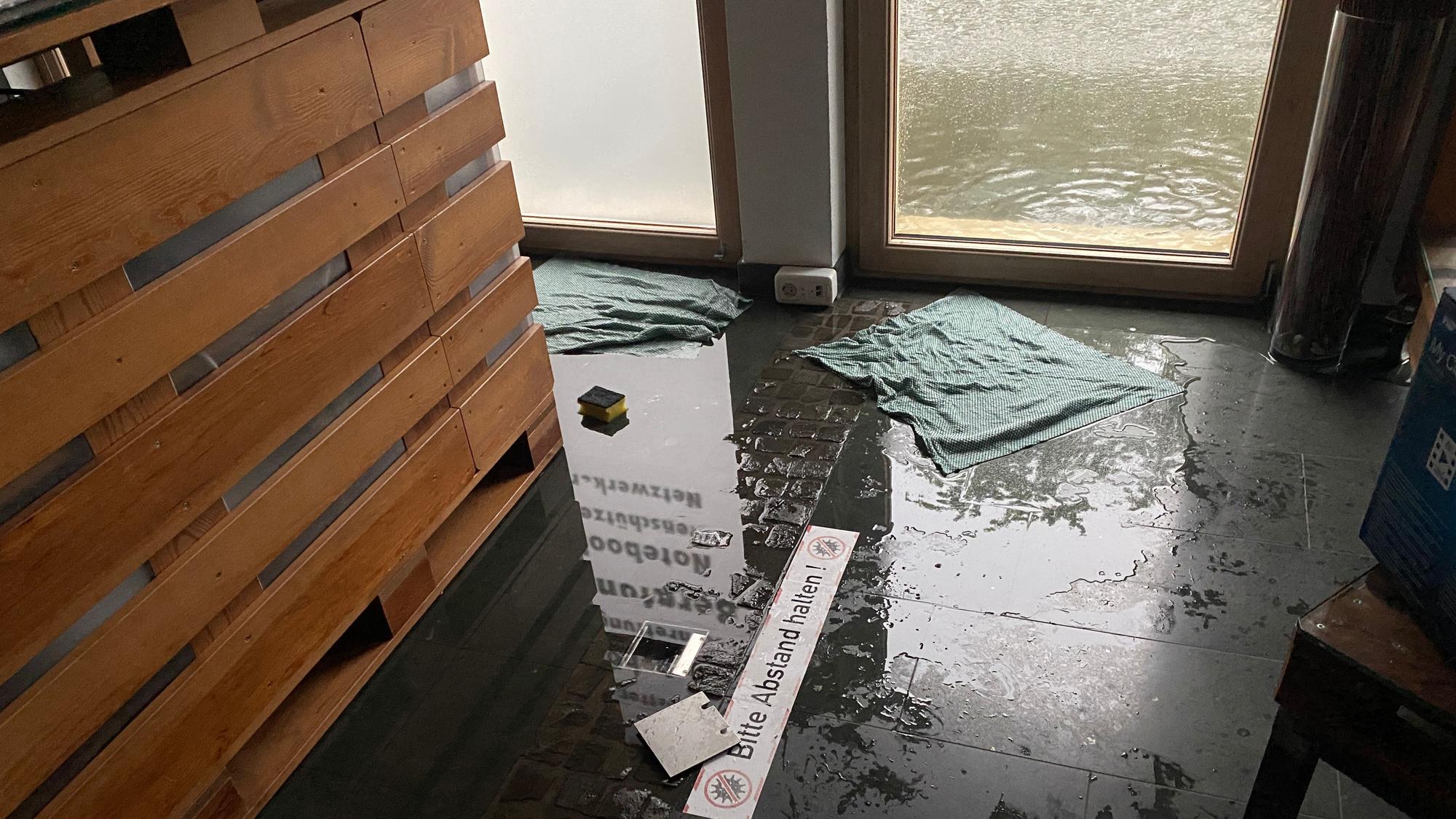 Auf dem Boden vor einer Eingangstür liegen feuchte Aufnehmer, draußen vor der Tür steht das Wassser.