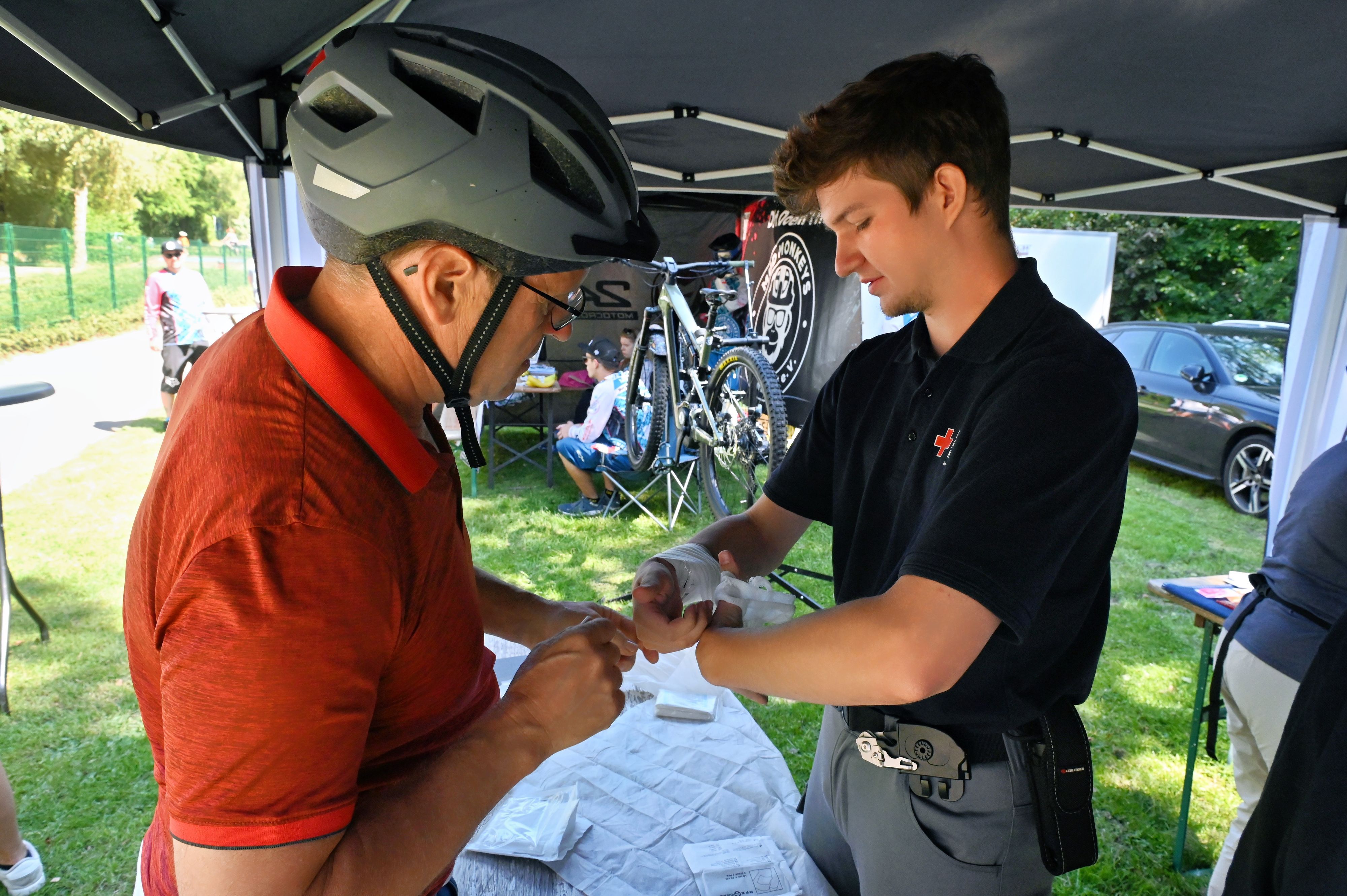 Noah Breidbach wickelt einen Verband um die Hand eines Bikers.