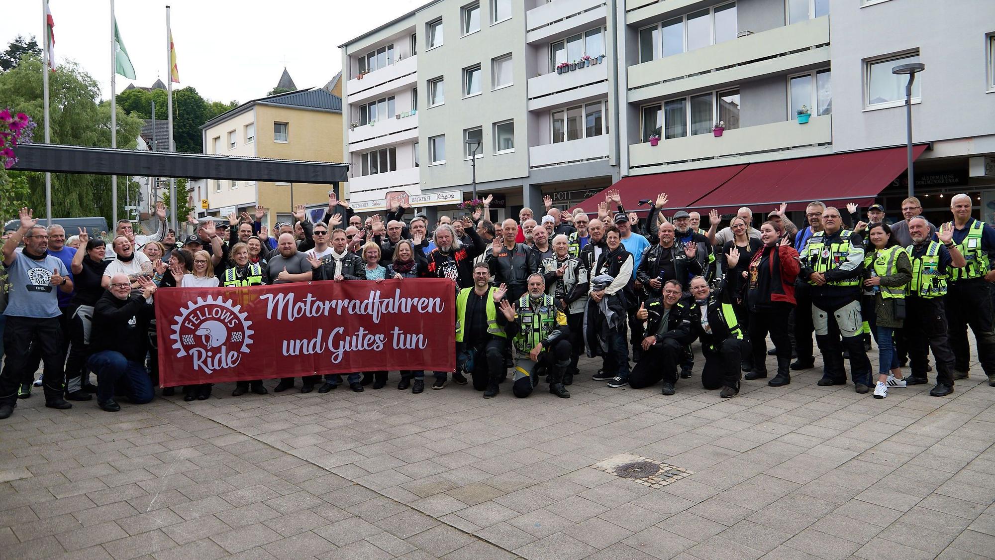 Eine große Gruppe Teilnehmer hat sich mit einem Transparent „Motorradfahren und Gutes tun“ in der Schleidener Innenstadt zum Gruppenbild aufgestellt.