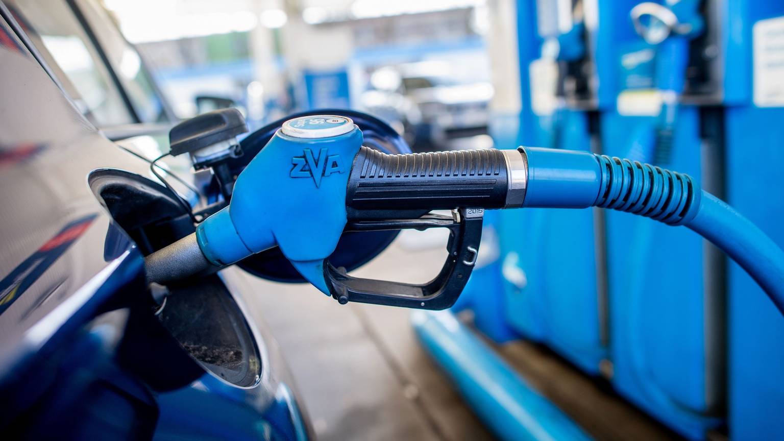 Eine Zapfpistole mit der Aufschrift „Super 95“ steckt an einer Tankstelle in der Tanköffnung eines Fahrzeugs.