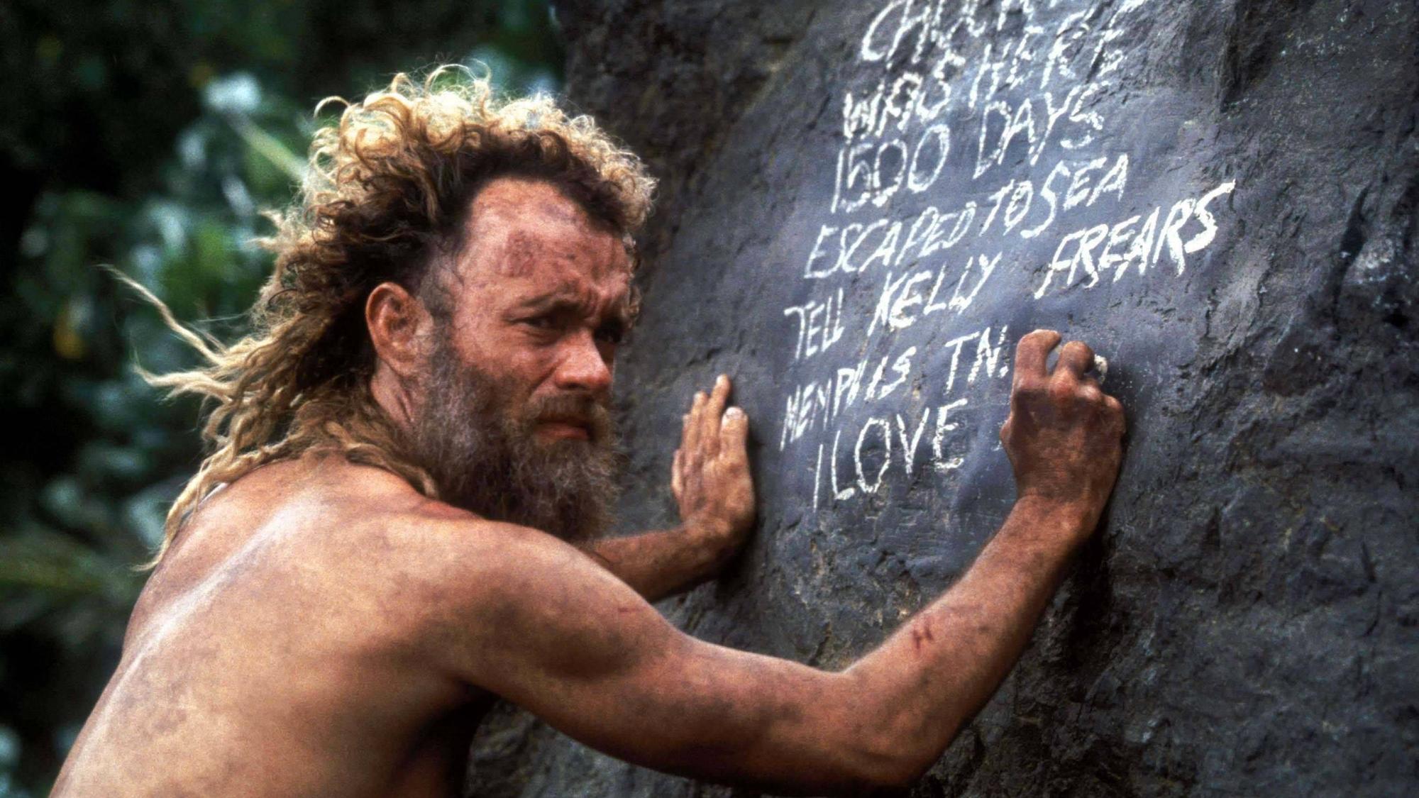 Tom Hanks schreibt mit Kreide auf einen Stein.