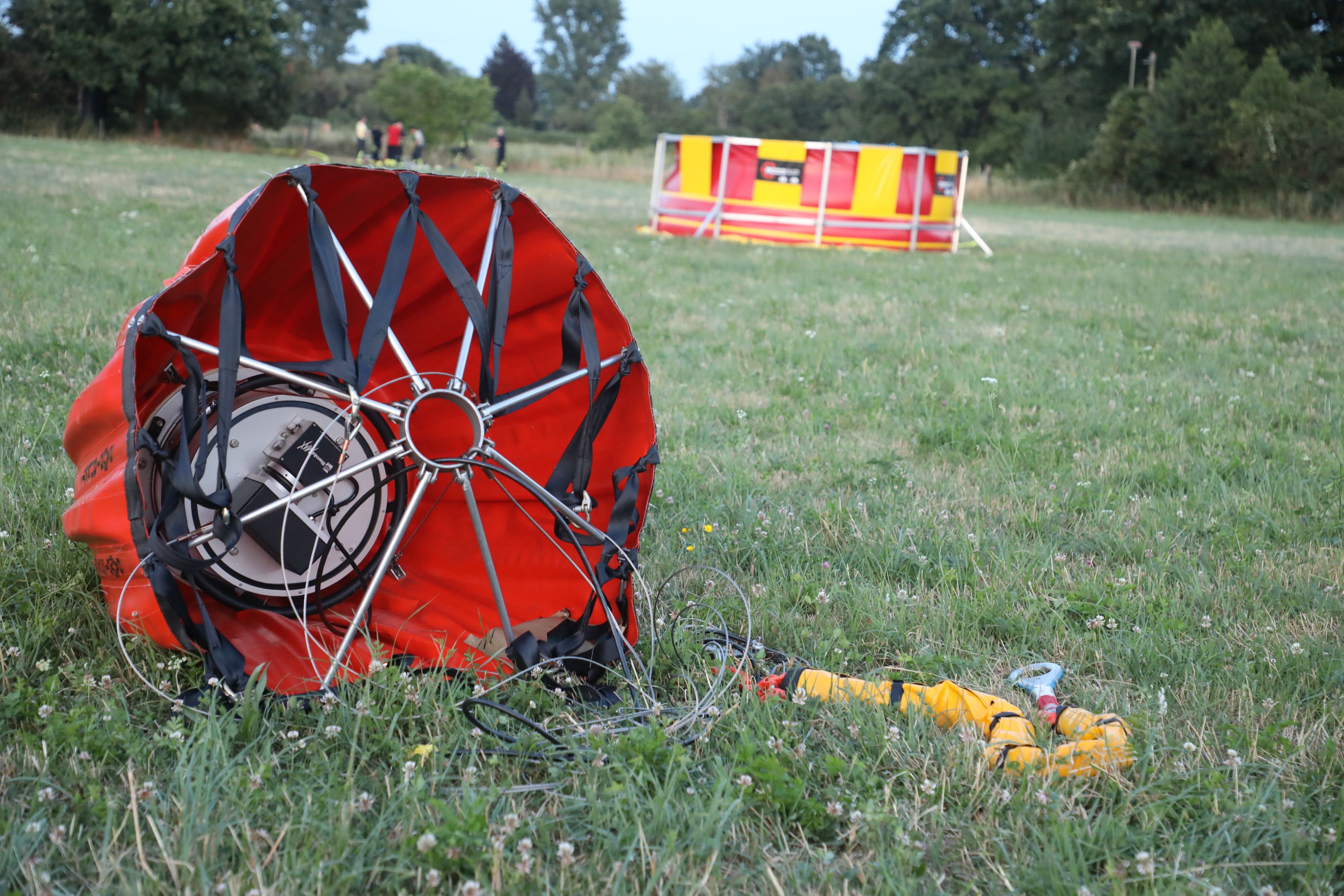 Ein „Bambi Bucket“ für die Brandbekämpfung liegt auf einer Weide, im Hintergrund ist ein Faltbecken der Feuerwehr zu sehen.