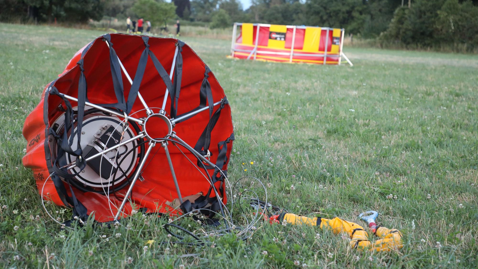 Ein „Bambi Bucket“ für die Brandbekämpfung liegt auf einer Weide, im Hintergrund ist ein Faltbecken der Feuerwehr zu sehen.