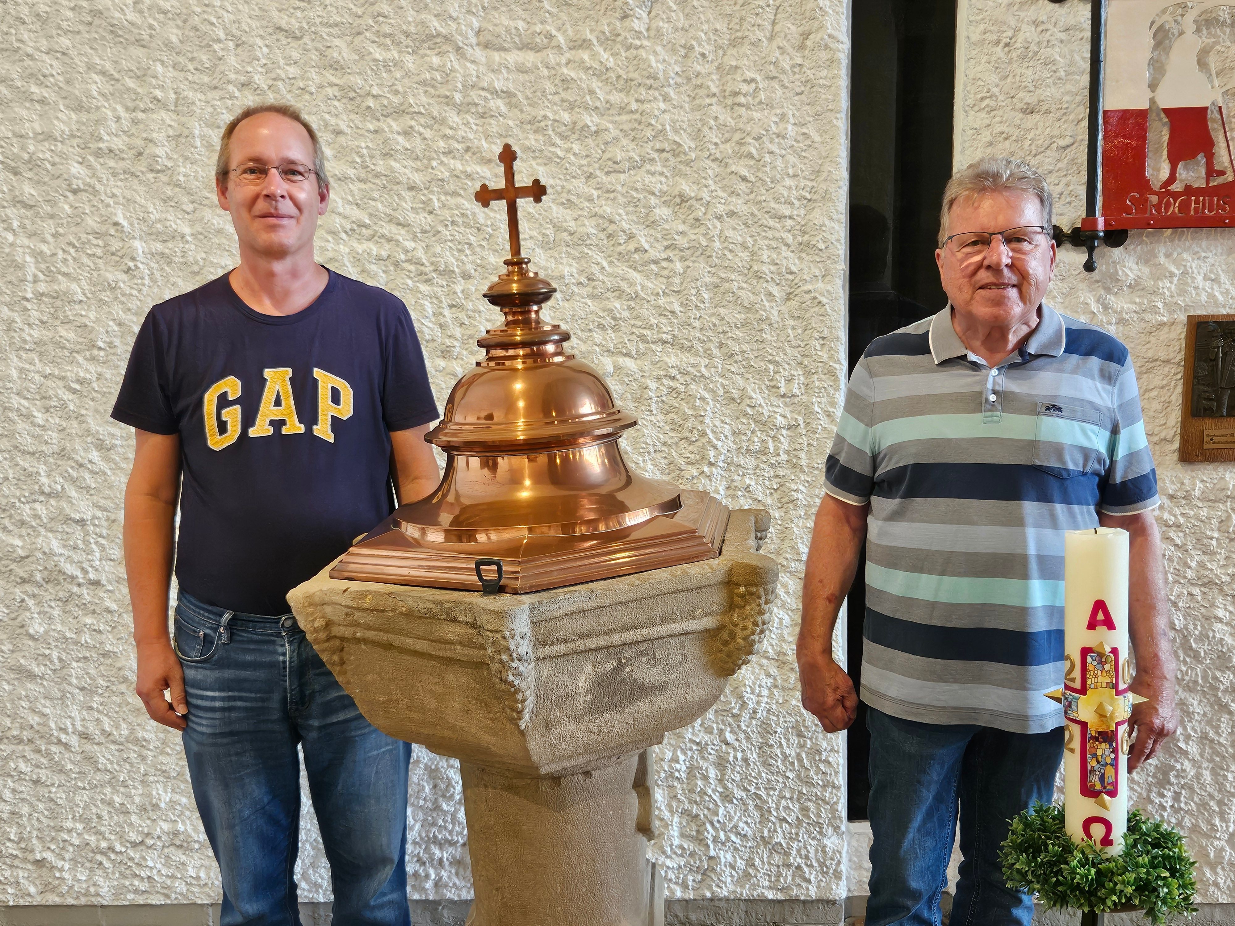 Wido Küpper (Kirchenvorstand) und Walter Sistig (ehemaliger Kirchenvorstand) stehen in T-Shirts neben einem Taufbecken.