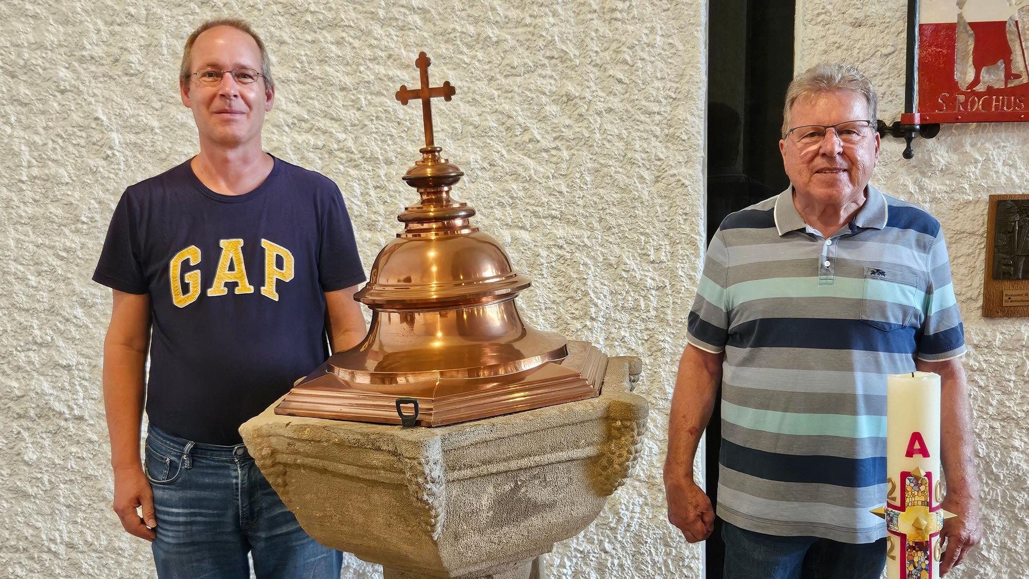 Wido Küpper (Kirchenvorstand) und Walter Sistig (ehemaliger Kirchenvorstand) stehen in T-Shirts neben einem Taufbecken.