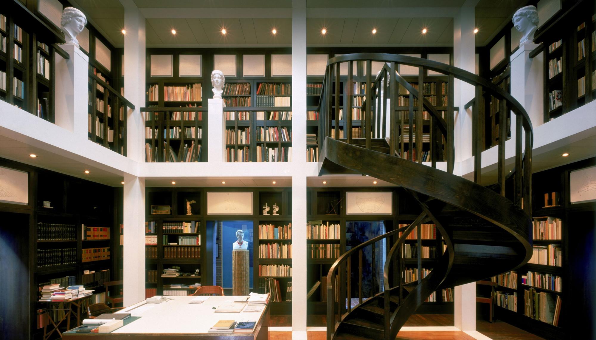 In einem Büro sind auf zwei mit einer Wendeltreppe verbundenen Etagen Bücherregale angeordnet.