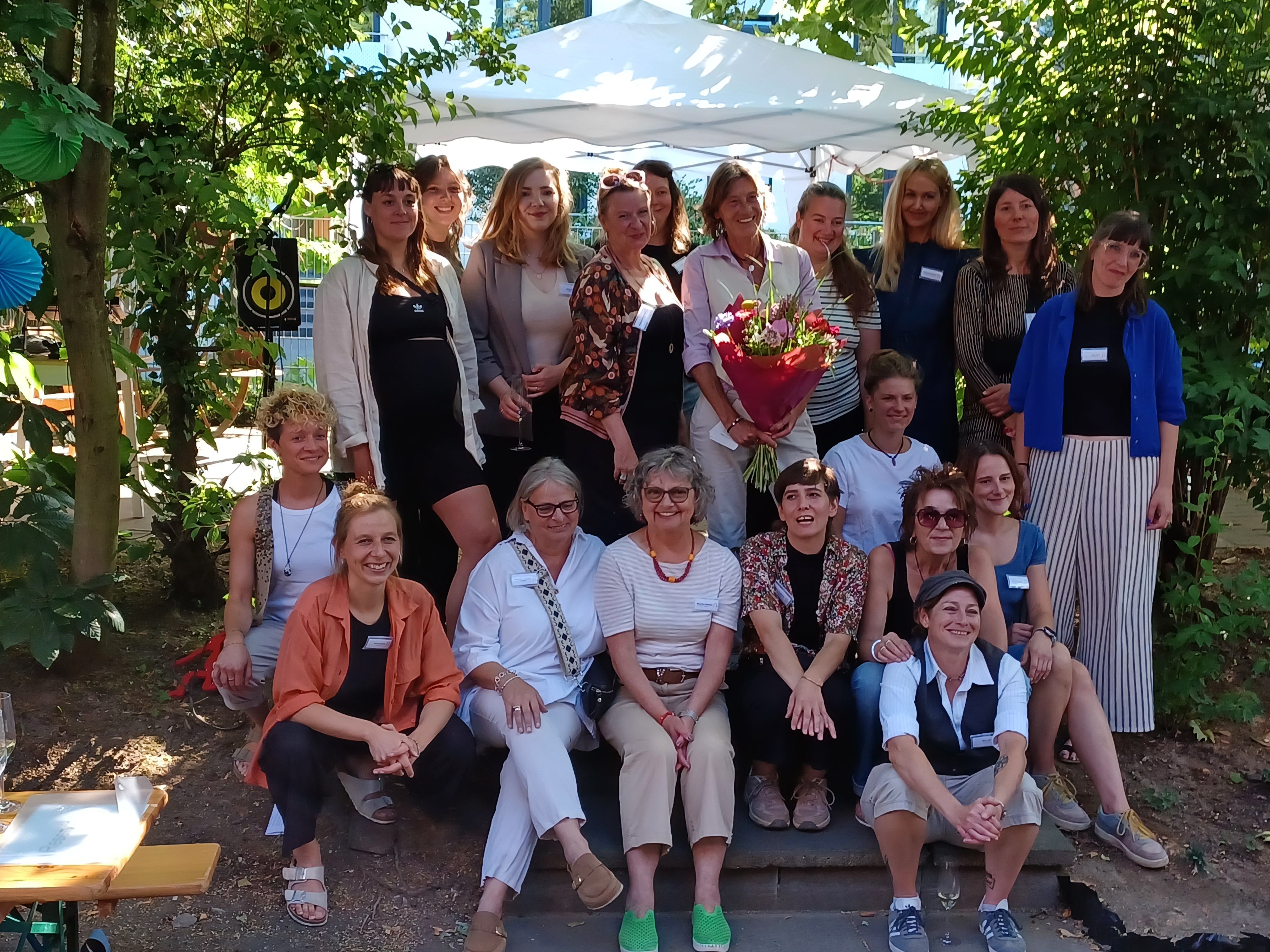 Eine Gruppe Frauen steht und sitzt in einem Garten.