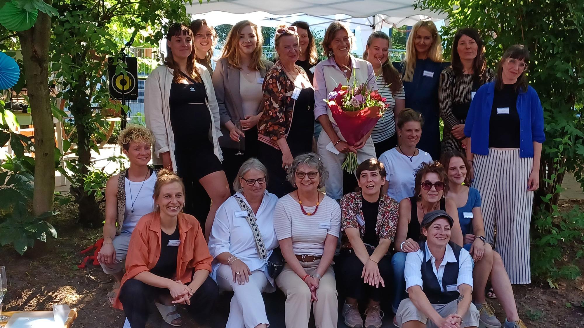 Eine Gruppe Frauen steht und sitzt in einem Garten.