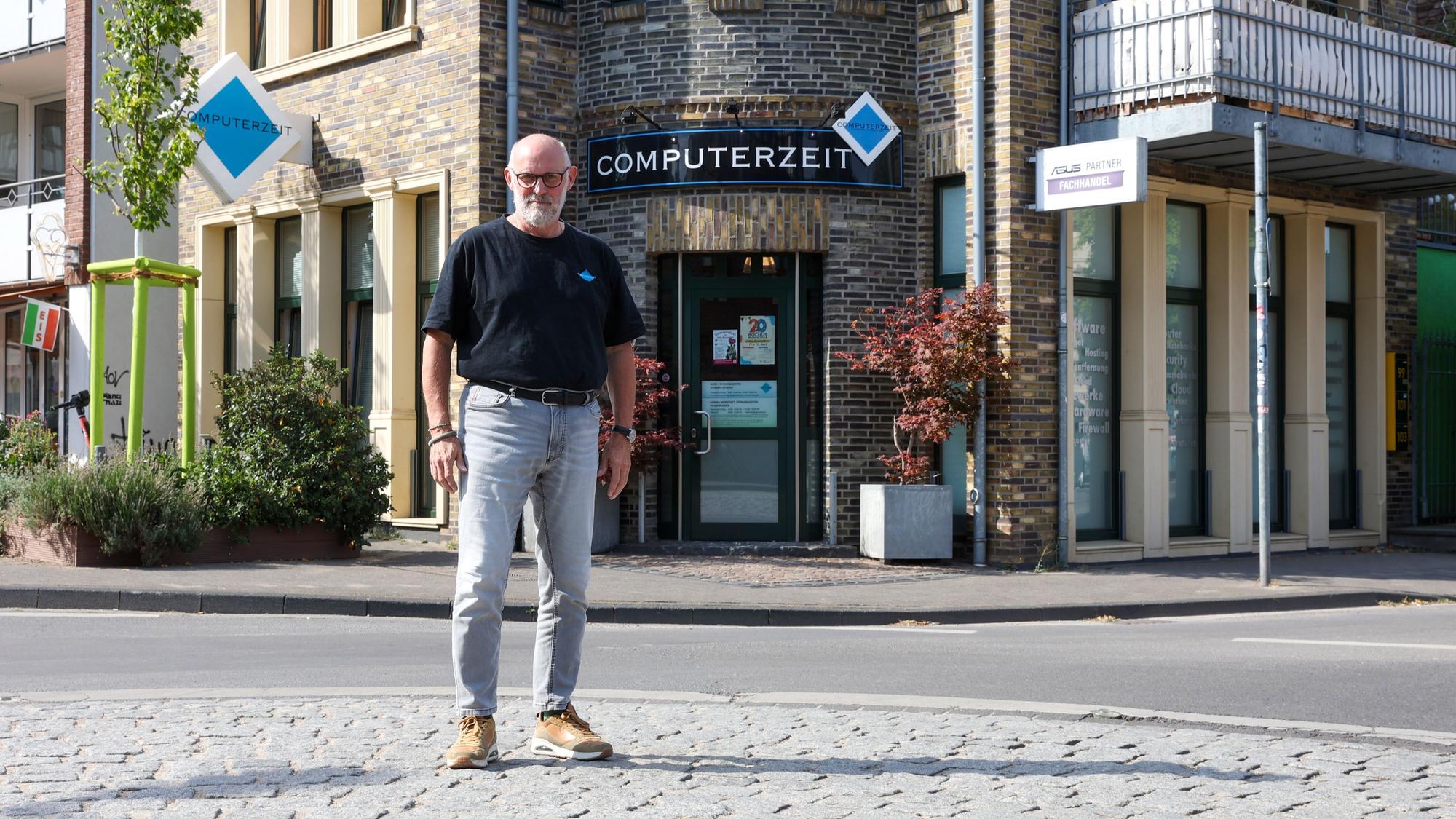 Ein Mann steht in der Mitte eines Kreisverkehrs. Hinter ihm ist sein Laden „Computerzeit“ zu sehen.