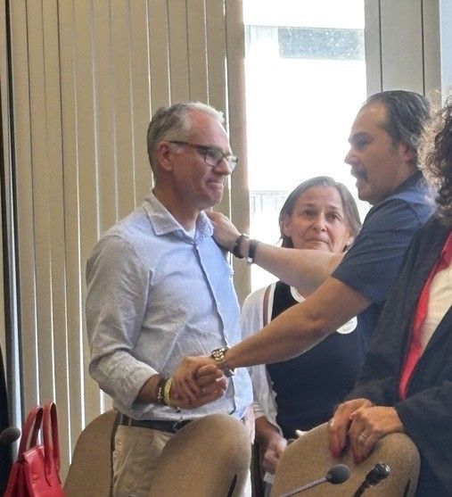 Auf dem Bild sind die Eltern von Luis Paulo und der Vater von Avin zu sehen, die sich umarmen.