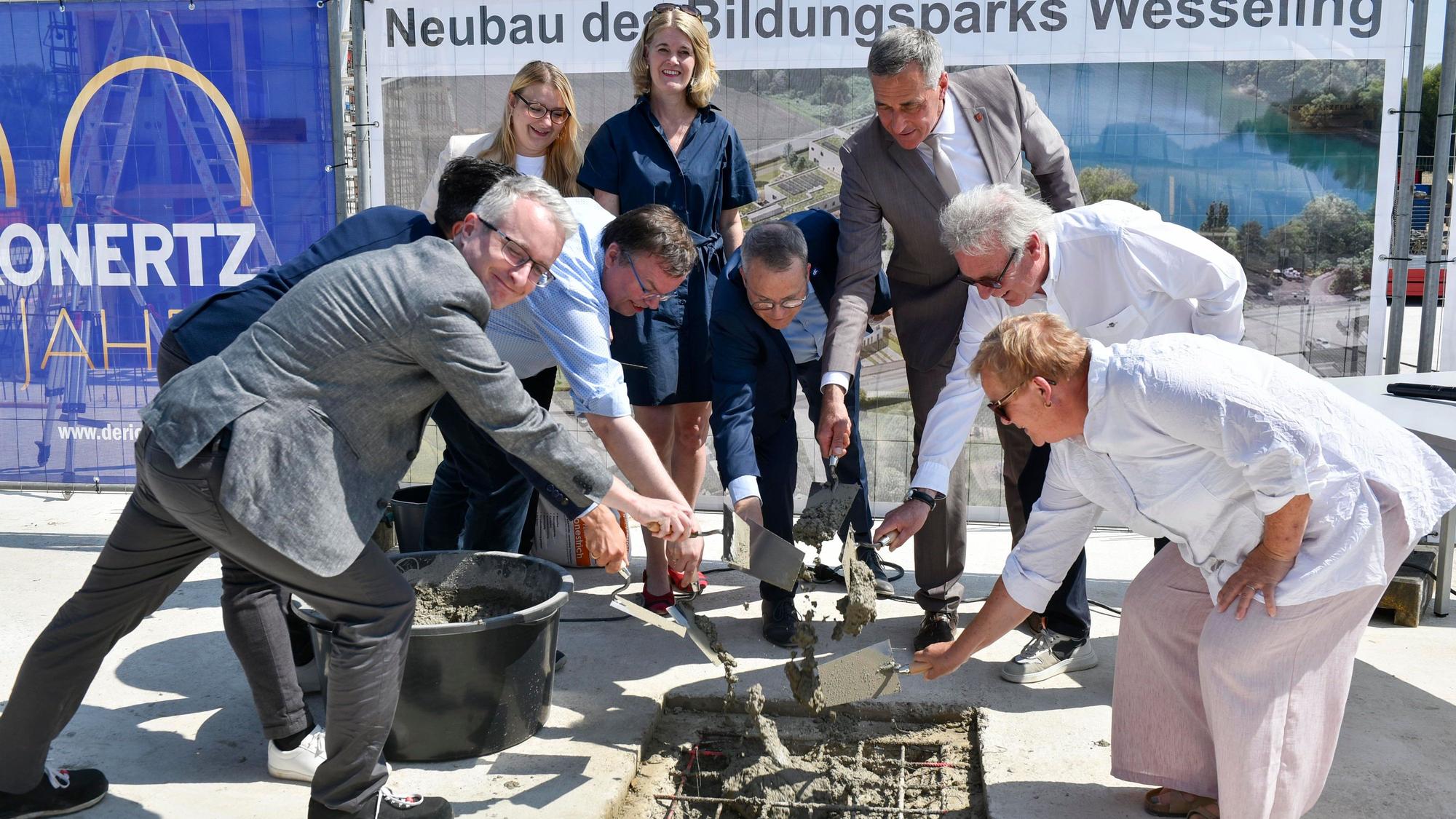 Mehrere Menschen beteiligen sich mit Kellen an einer Grundsteinlegung.
