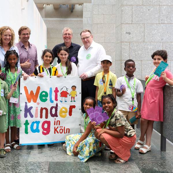 Neun Jungen und Mädchen des Linoclub-Kinderrates stehen gemeinsam mit Isabella Neven DuMont (wir helfen e.V.), Lars Hüttler (Kinderschutzbund Köln), Hans-Josef Saxler (Soziales Zentrum Linoclub) und Oberbürgermeister Torsten Burmester im Flur des Historischen Rathauses. Sie halten einen großes Weltkindertag-Plakat in den Händen.