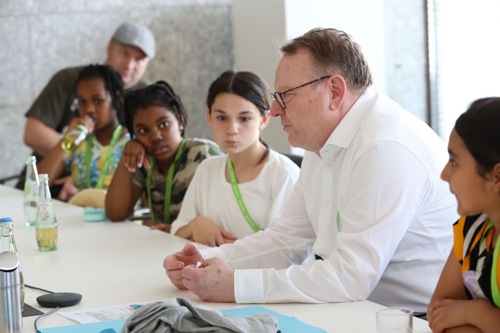 Kölns Oberbürgermeister Torsten Burmester sitzt in ein weißes Hemd gekleidet an einem großen Konferenztisch im Historischen Rathaus, neben ihm sitzen drei Mädchen vom Kinderrat des Linoclubs in Lindweiler.