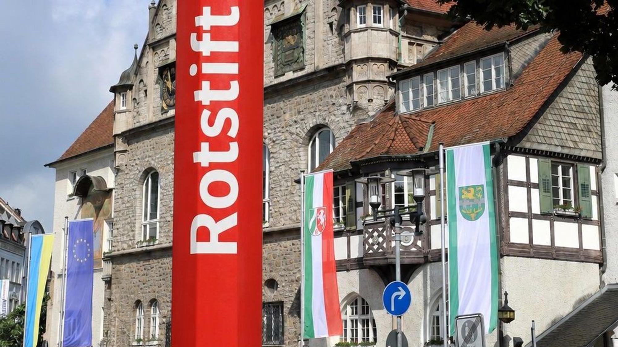 Die Fotomatage zeigt einen roten Stift vor dem Rathaus.