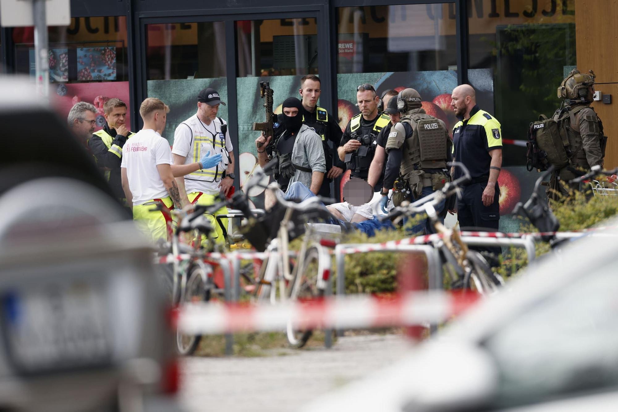 Einsatzkräfte stehen vor einem Supermarkt neben einer verletzten Person auf einer Trage. In dem Supermarkt im Süden Berlins hielt ein Mann seit dem späten Freitagabend eine Frau als Geisel.