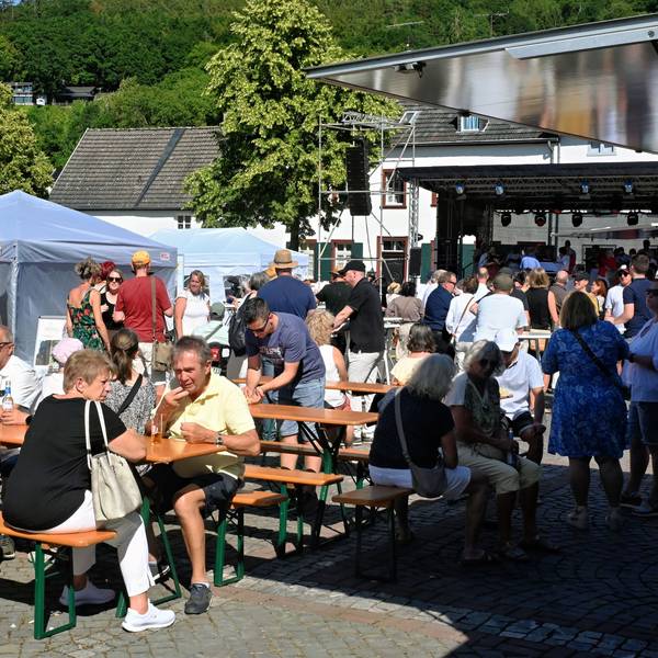 Beim Helferfest zum fünften Jahrestag der Flut in Bad Münstereifel sitzen Besucherinnen und Besucher vor der Bühne an Biertischen zusammen.