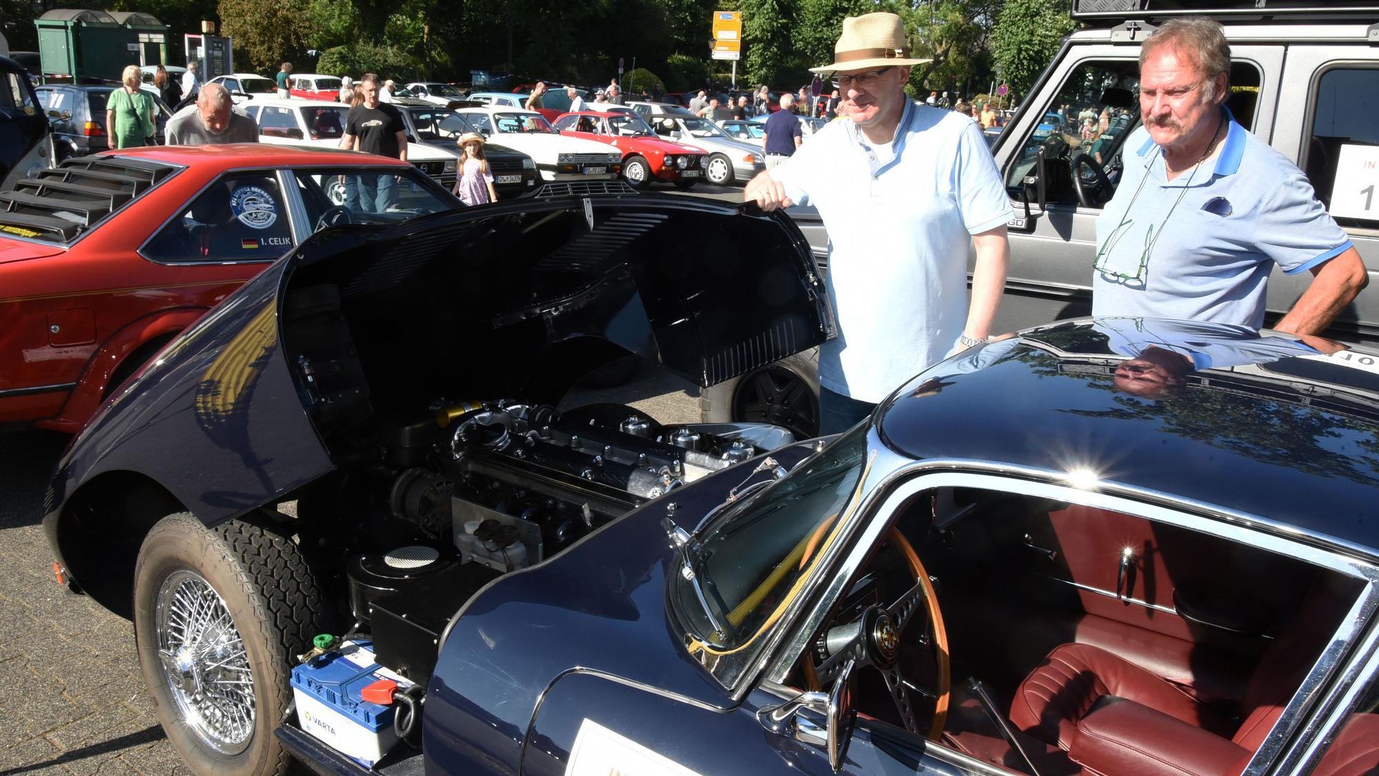 Zahlreiche Oldtimer-Autos stehen auf einem Platz, ein Jaguar hat die Motorhaube geöffnet.