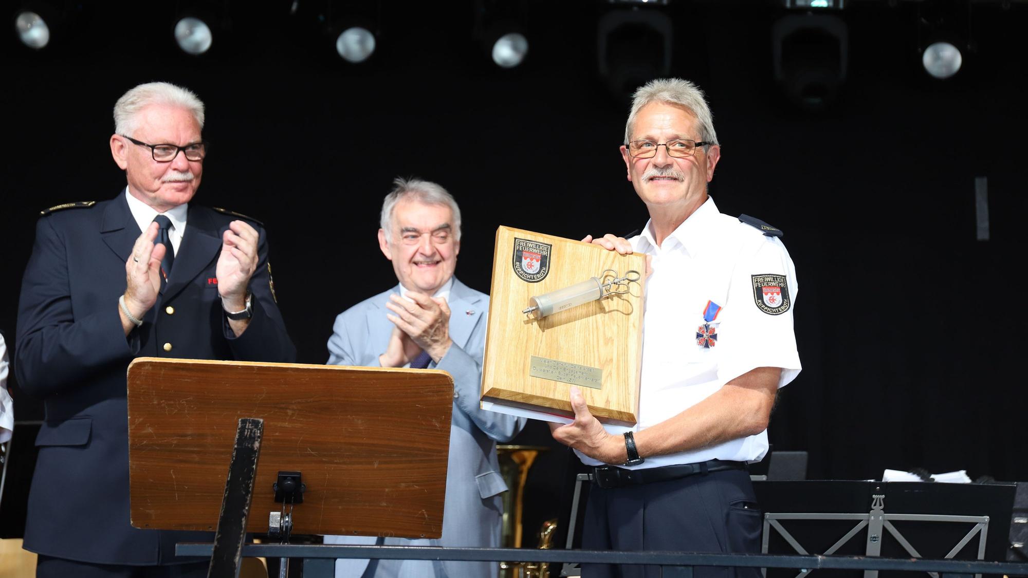 Feuerwehrarzt Dr. Herbert Broich (r.) erhielt vom Löschzug Winterscheid zum Abschied eine alte, große Spritze. Kreisbrandmeister Stefan Gandelau (l.) und Innenminister Herbert Reul (M.) applaudieren.