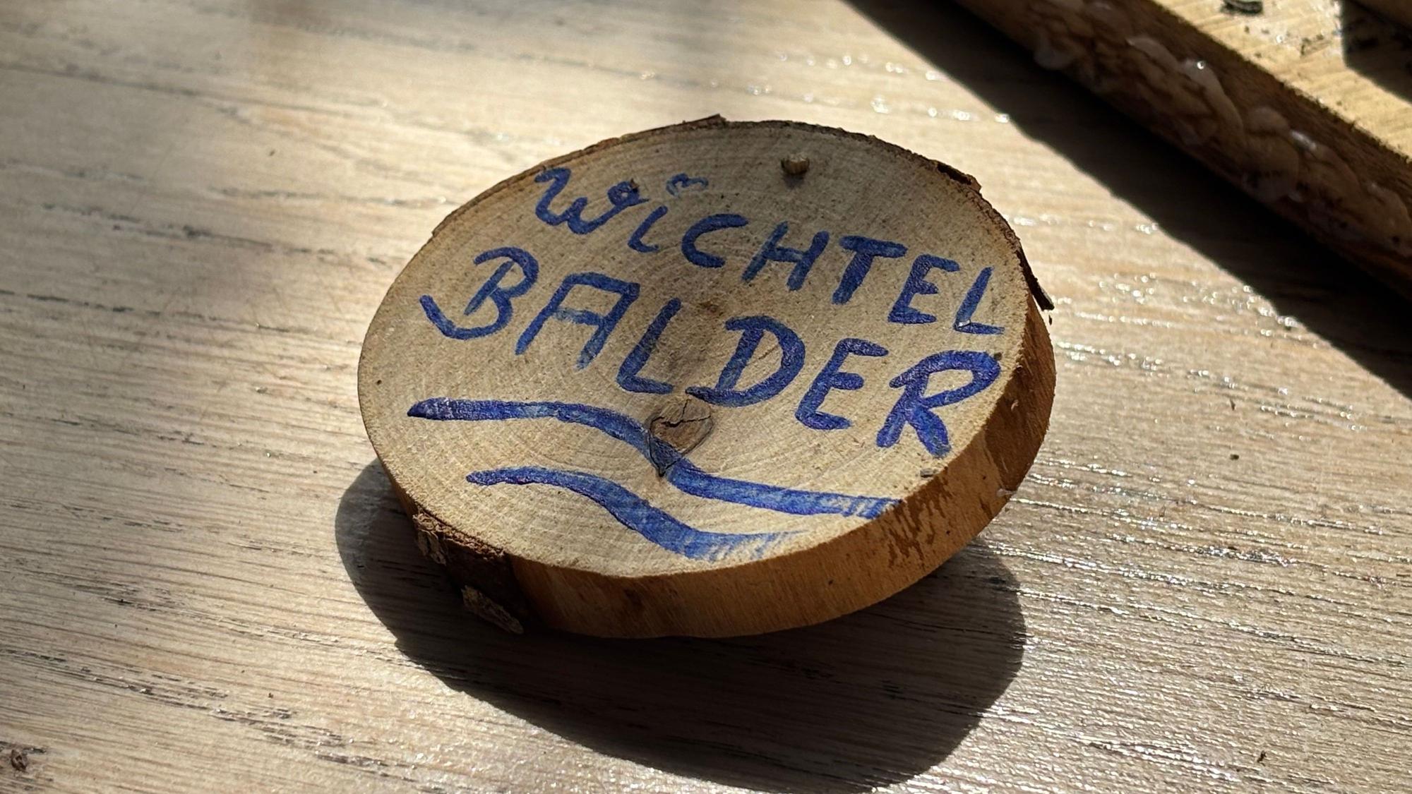 Detailaufnahme auf das runde Namensschild „Wichtel Balder“, das auf einem Holztisch liegt