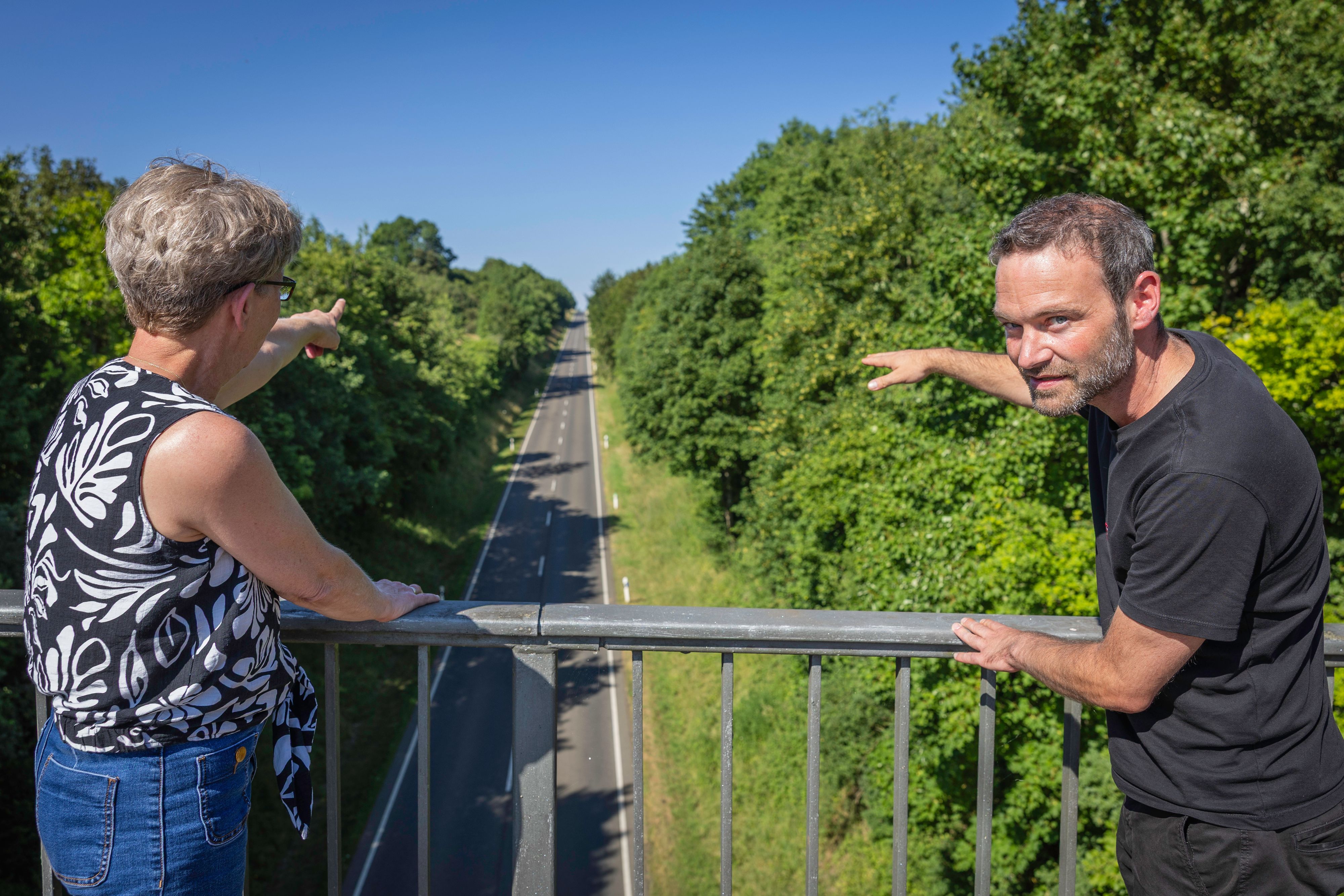 Schmitz und Mandl blicken von einer Brücke auf die den Berg hinabführende L206.