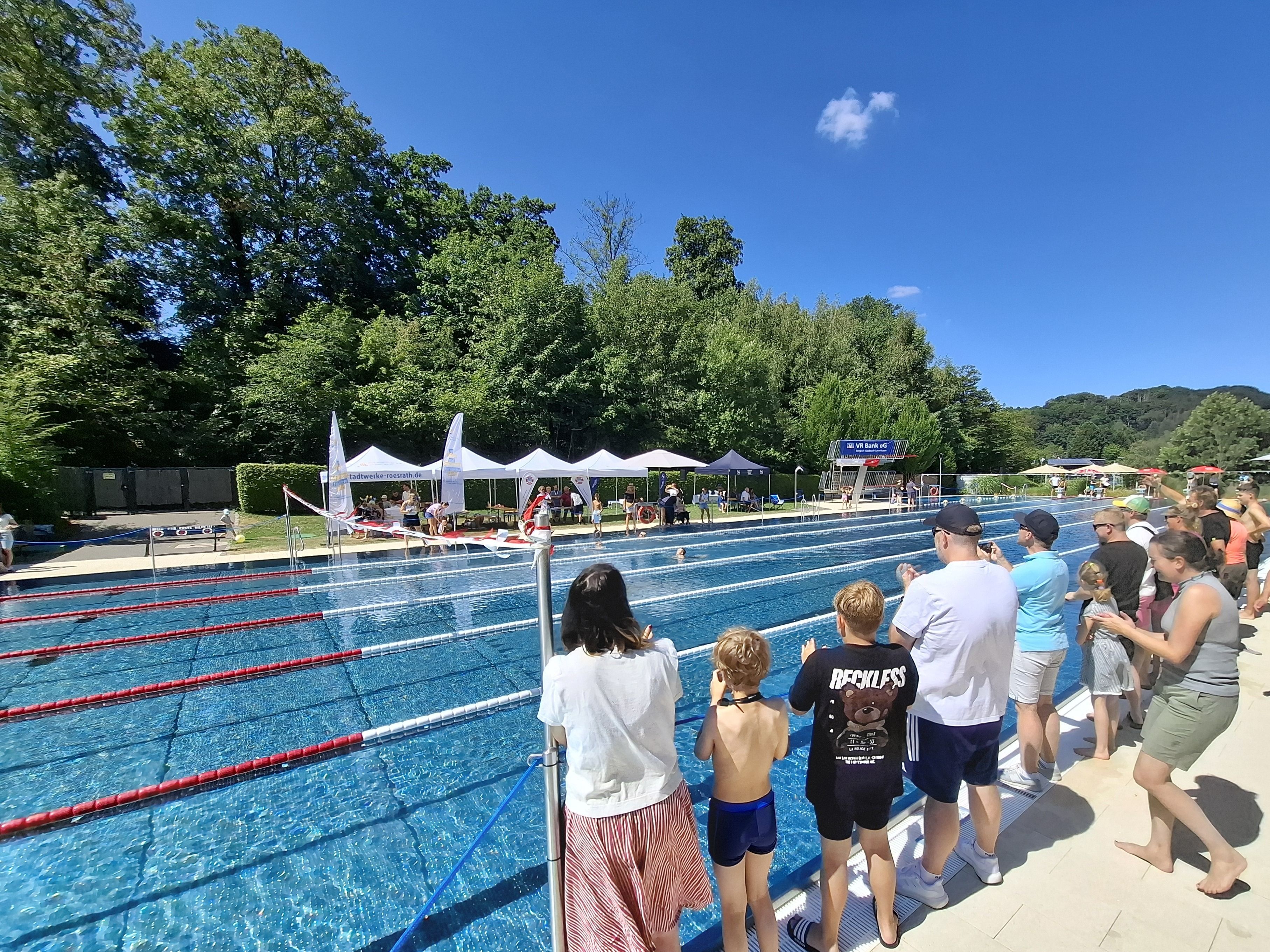 Menschen stehen am Rand des Schwimmbeckens im Freibad und feuern die Schwimmer an.