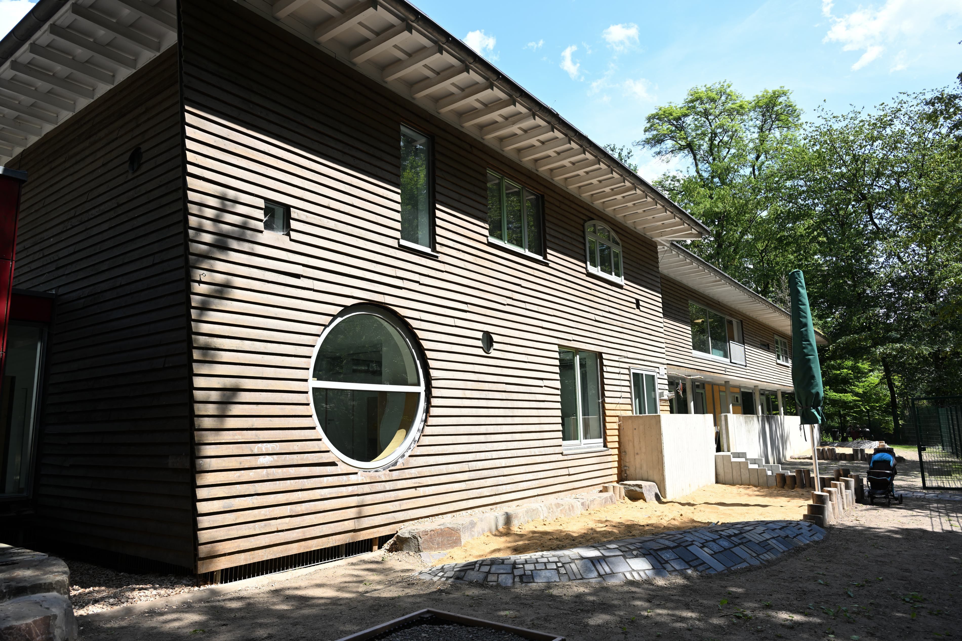 Ein moderner Holzbau mit begrüntem Dach. Davor noch eine sandige Baustelle.
