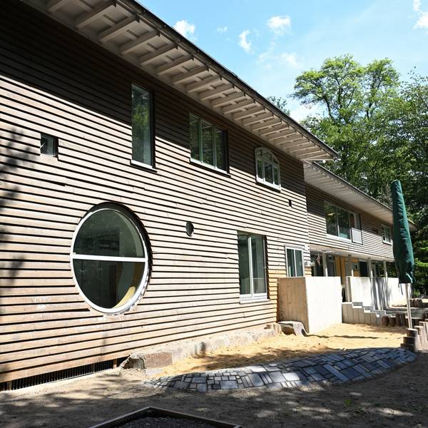 Ein moderner Holzbau mit begrüntem Dach. Davor noch eine sandige Baustelle.