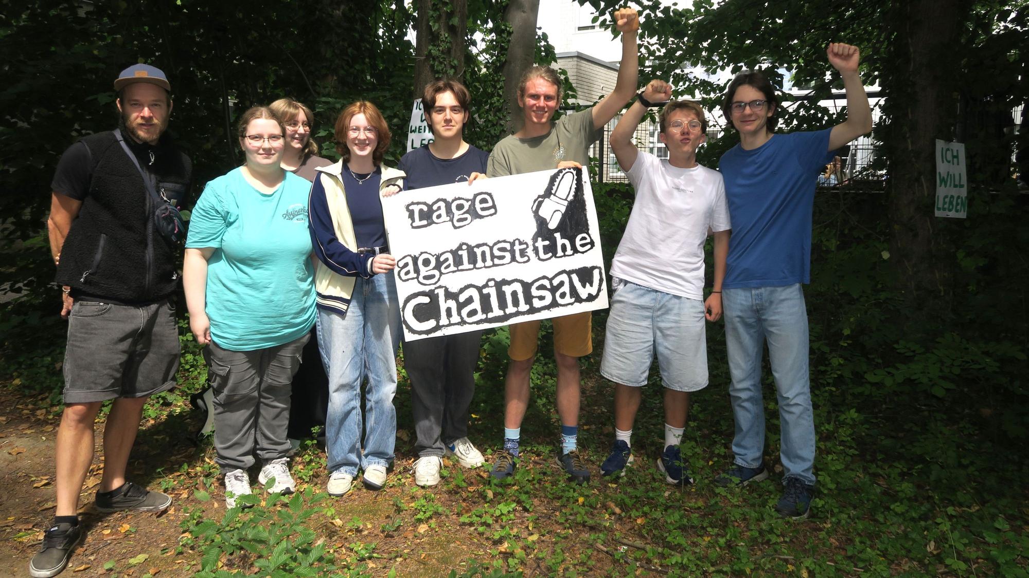 Schüler stehen vor Bäumen und halten ein Plakat hoch: „Rage against the chainsaw“ - Wut gegen die Kettensäge.