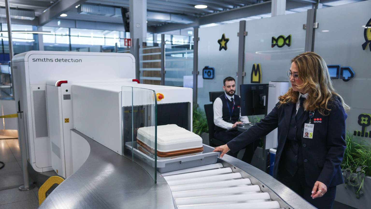Die Mitarbeiterin einer Sicherheitsfirma schiebt im Sicherheitsbereich am Flughafen Köln/Bonn einen Koffer in einen Scanner. Eine neue Anlage mit elf modernen CT-Kontrollspuren und Scannern soll künftig für schnellere, komfortablere und effizientere Abläufe sorgen.