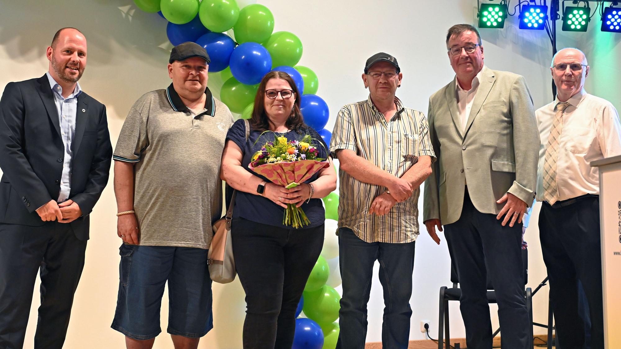 Fünf Männer und eine Frau, die Blumen in der Hand hat, stehen in einer Reihe.