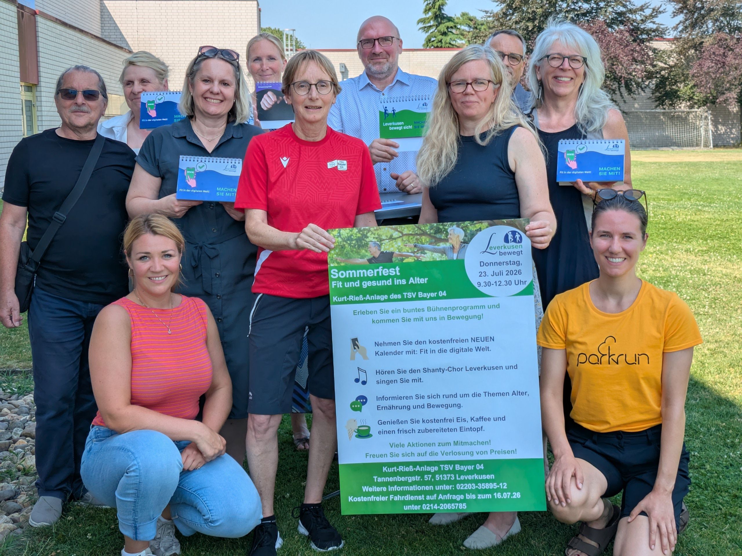 Männer und Frauen halten ein Plakat für ein Sommerfest in die Höhe.