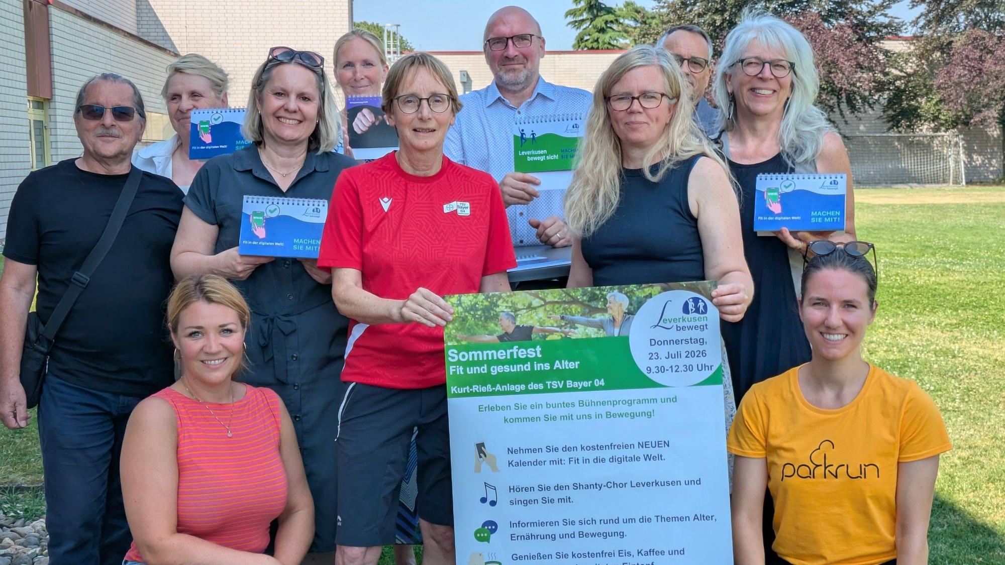 Männer und Frauen halten ein Plakat für ein Sommerfest in die Höhe.